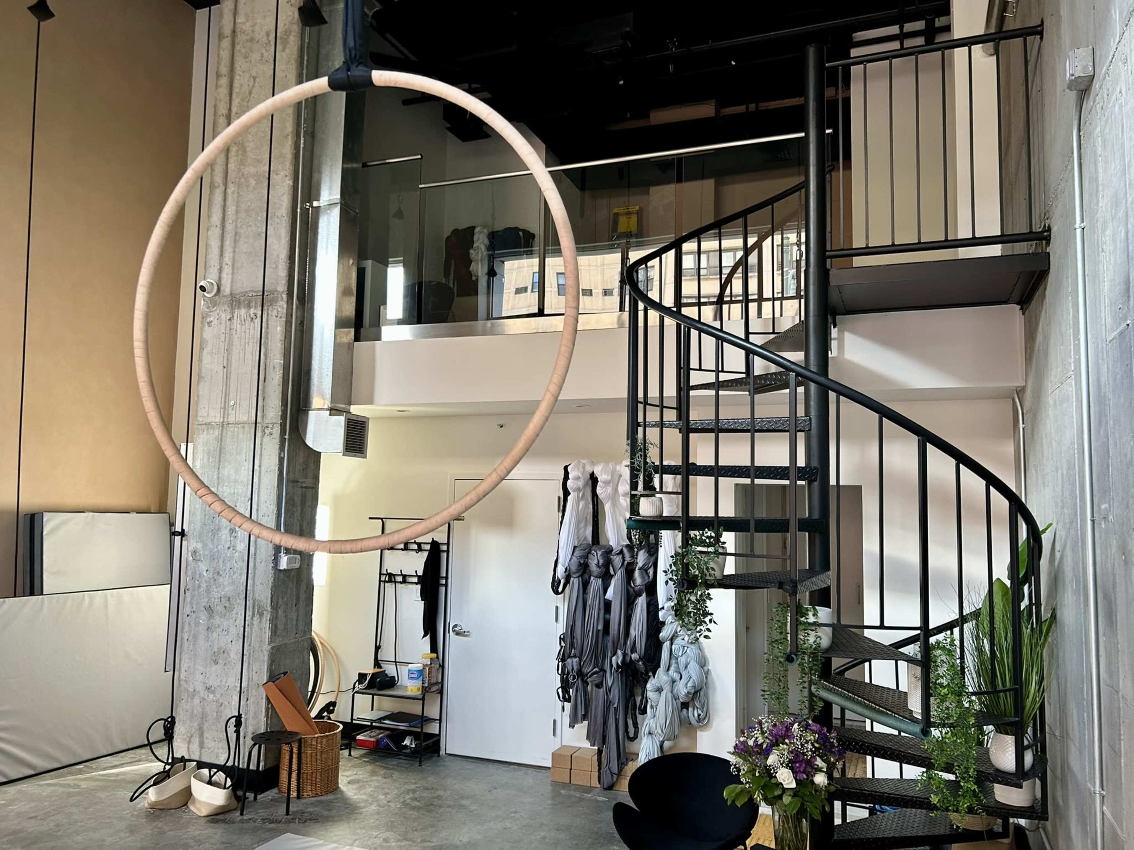 The image shows a spacious interior with a spiral staircase, a hanging hoop, and various artistic props arranged around a minimalist design.
