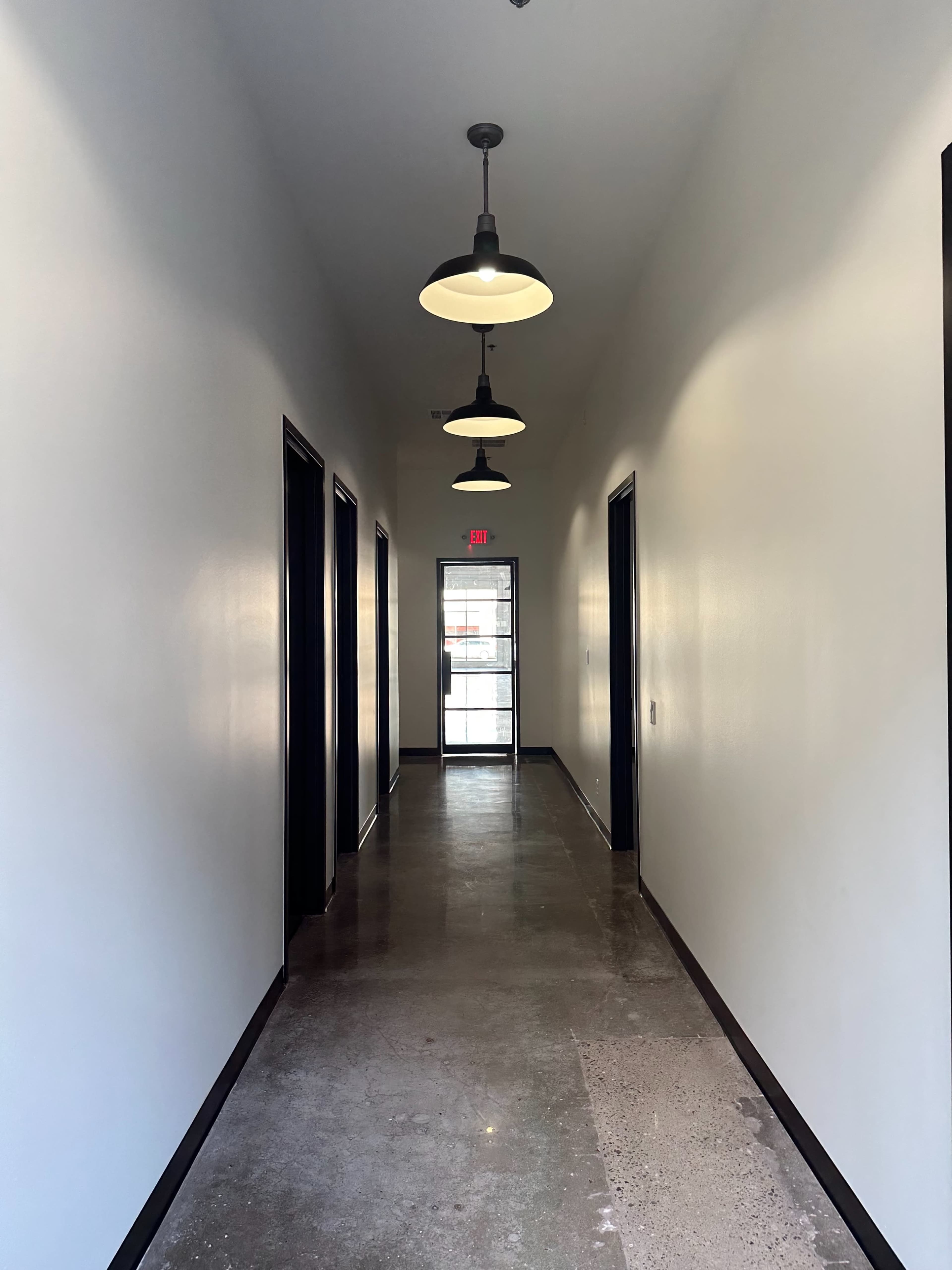 A long, narrow hallway with several doorways on each side and a glass door at the end leading outside.