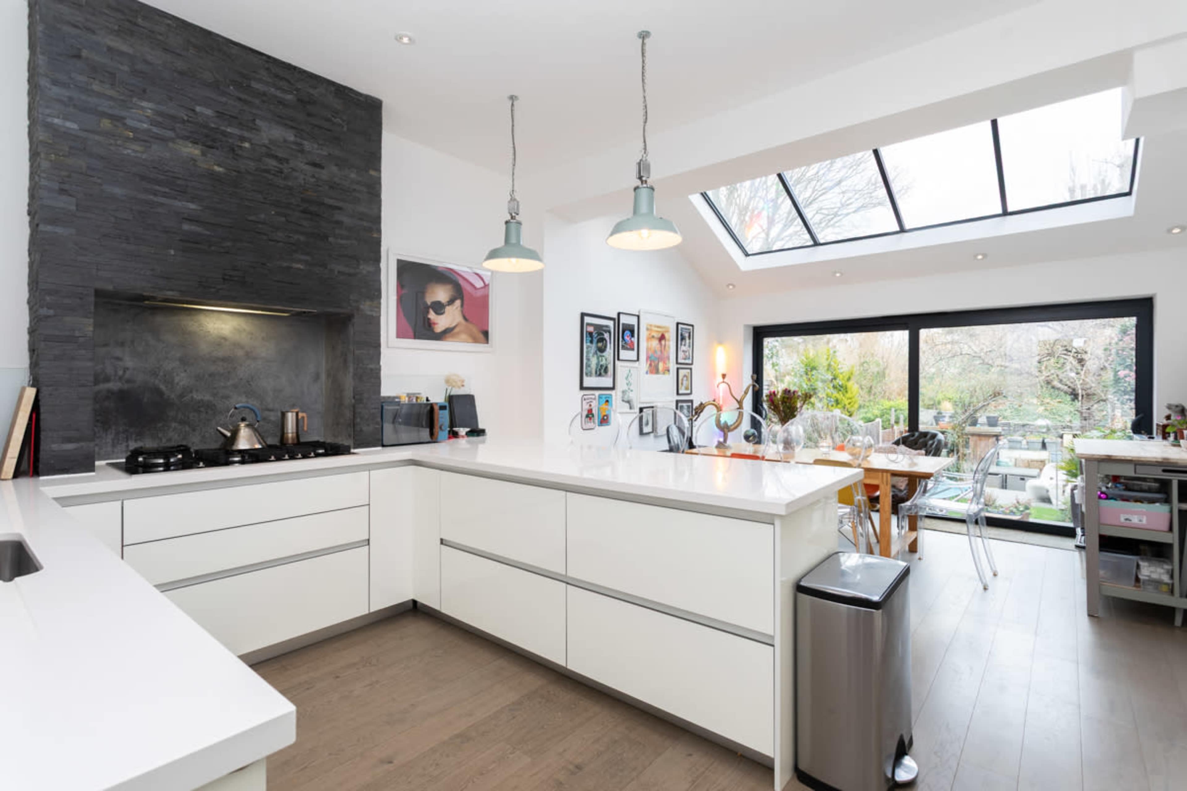The modern kitchen features a minimalist design with sleek white cabinetry, a dark stone backsplash, and large windows that provide natural light and outdoor views.