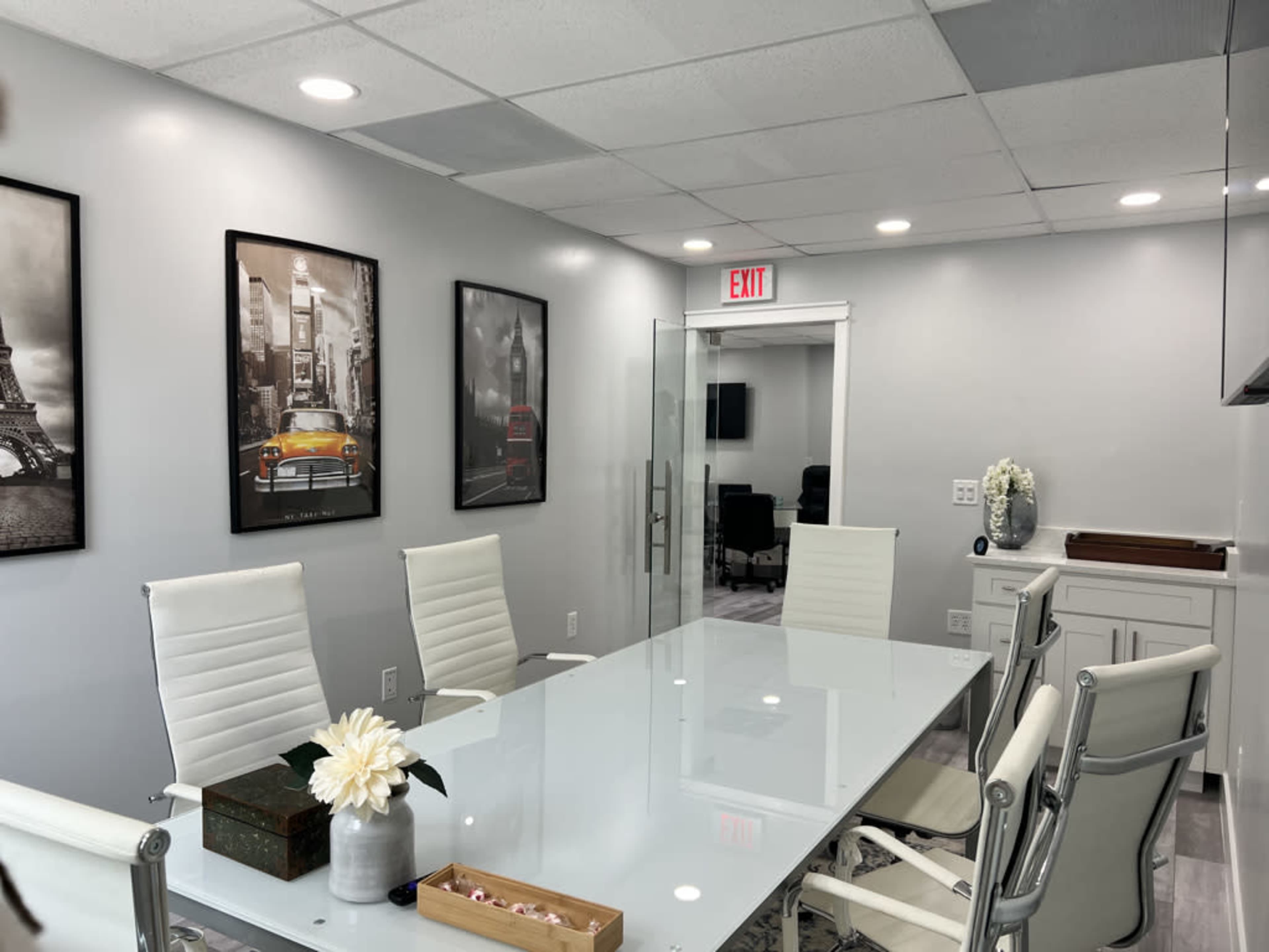A modern conference room with a glass table surrounded by white chairs and framed black-and-white photographs on the walls.