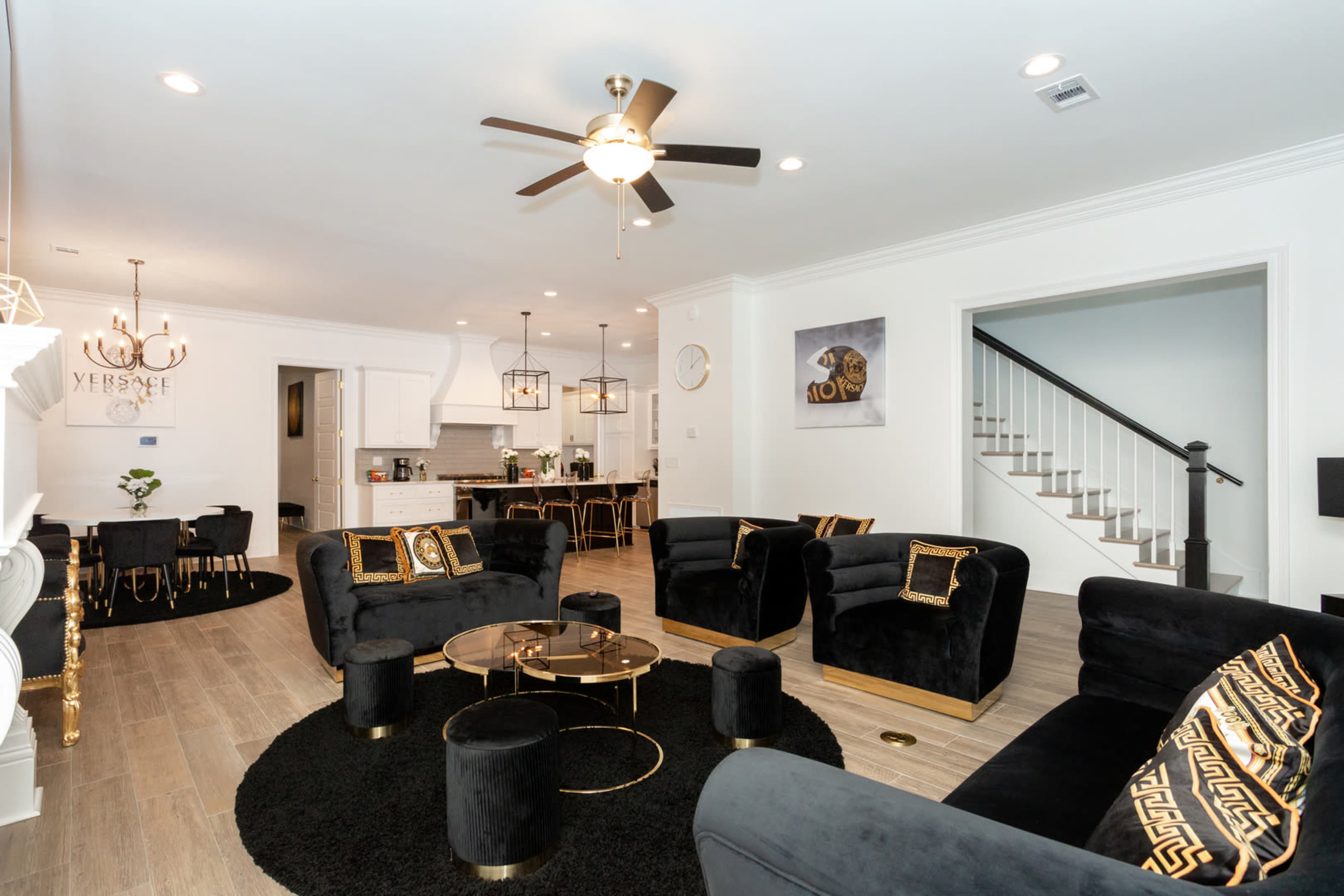 A modern living room featuring black upholstered furniture, a circular black rug, a glass coffee table, and a staircase leading to an upper floor.