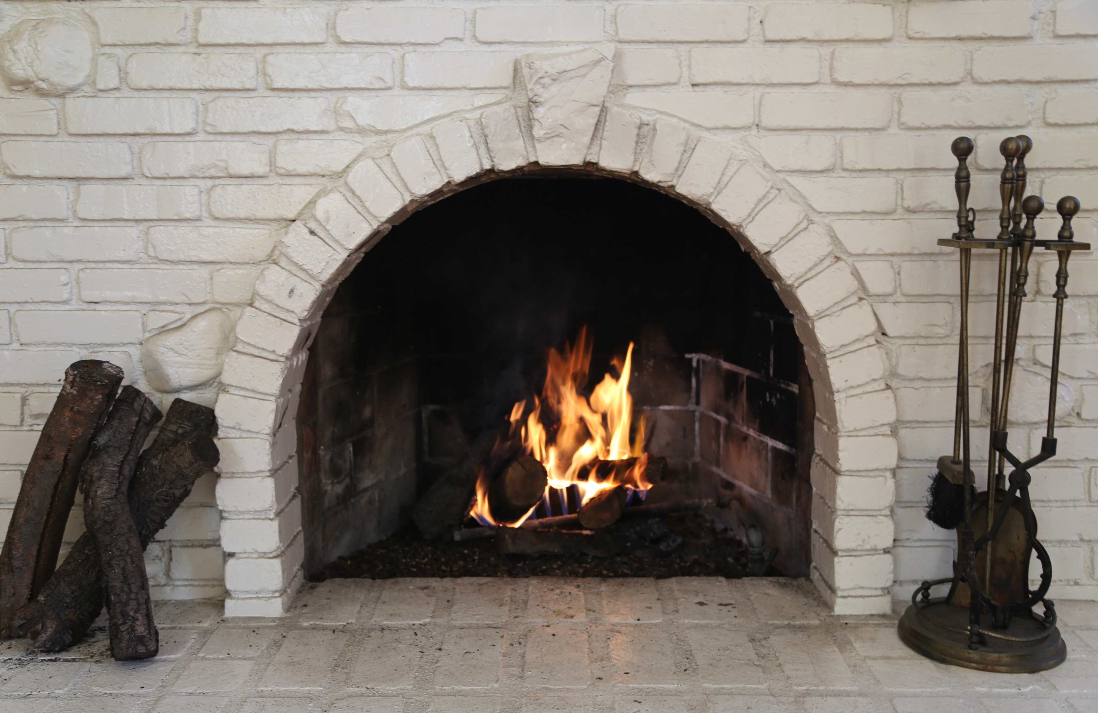 A brick fireplace with a roaring fire and a stack of logs on the side.