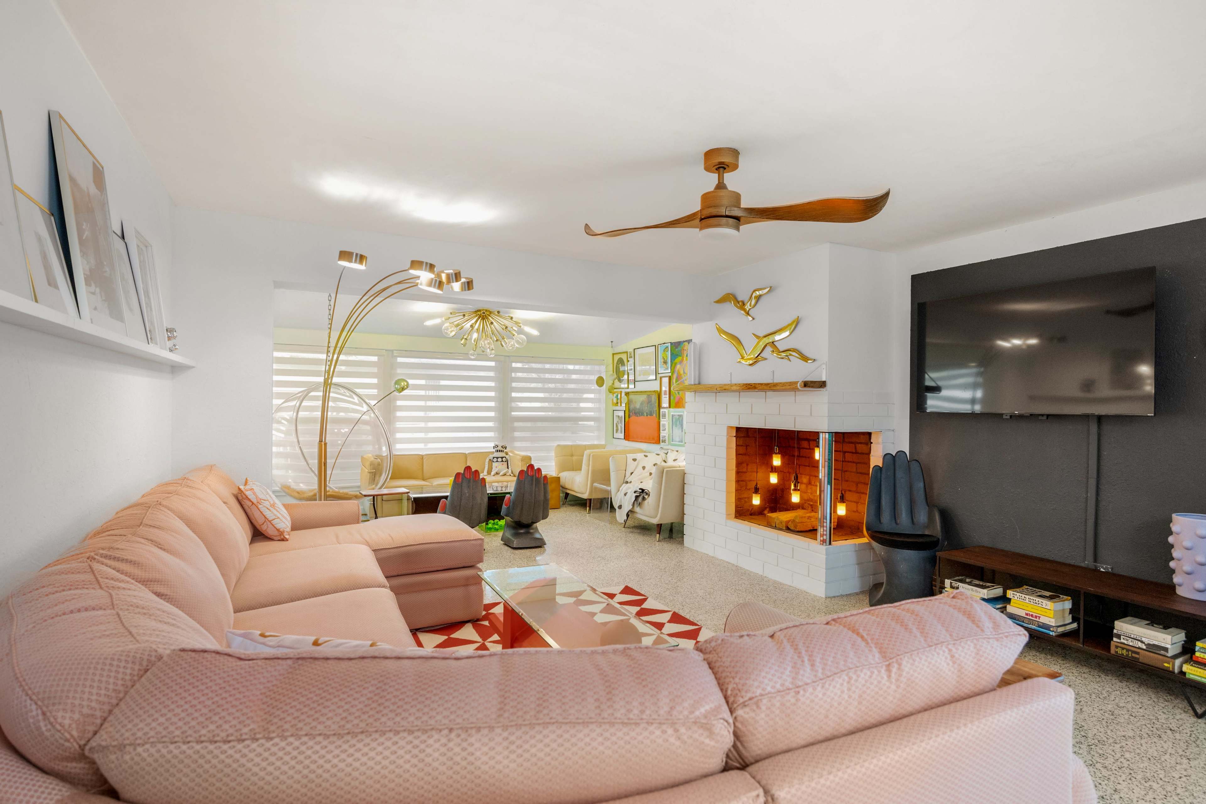 A spacious living room features a pink sectional couch, a mounted television, and a cozy fireplace with a modern fan overhead.