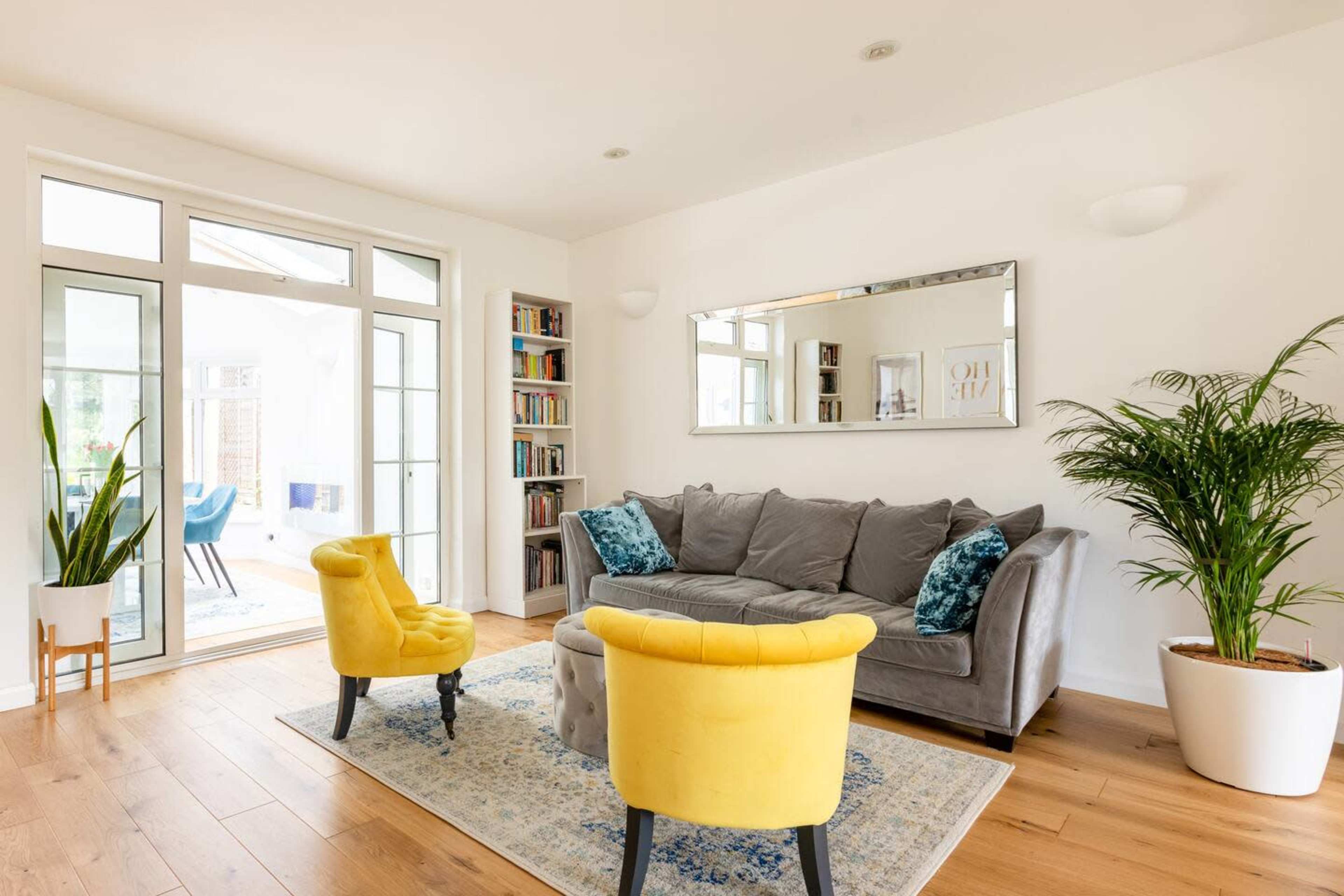 A modern living room with a gray sofa, two yellow chairs, a potted plant, and a bookshelf, along with large glass doors leading to an outdoor area.