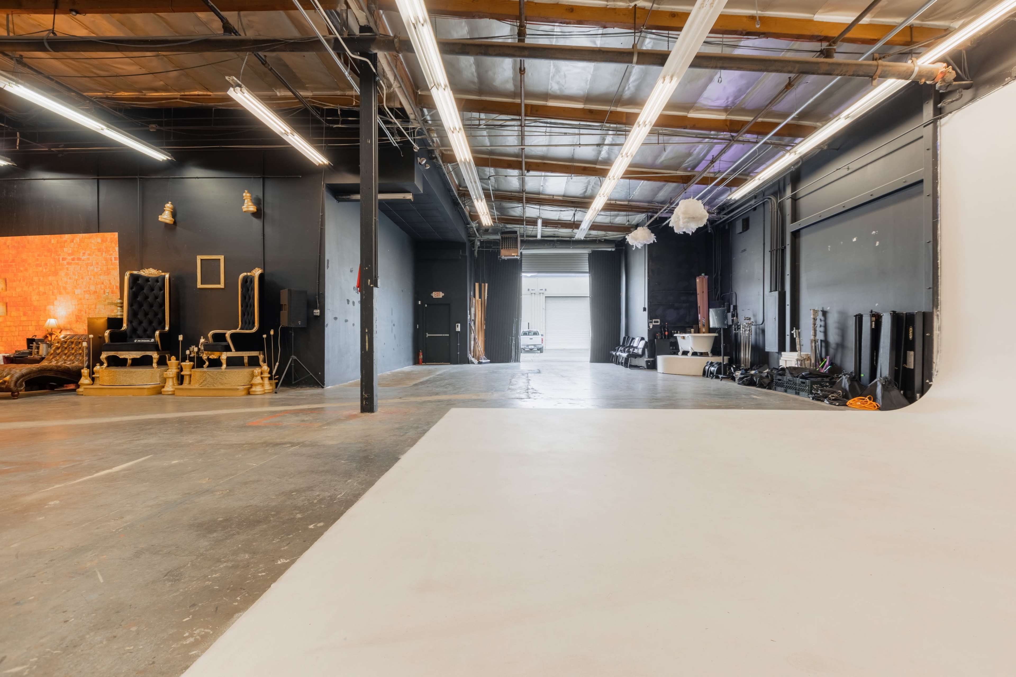 The image shows a spacious studio with a large, empty area and various equipment along the sides, including a backdrop and seating in a corner.