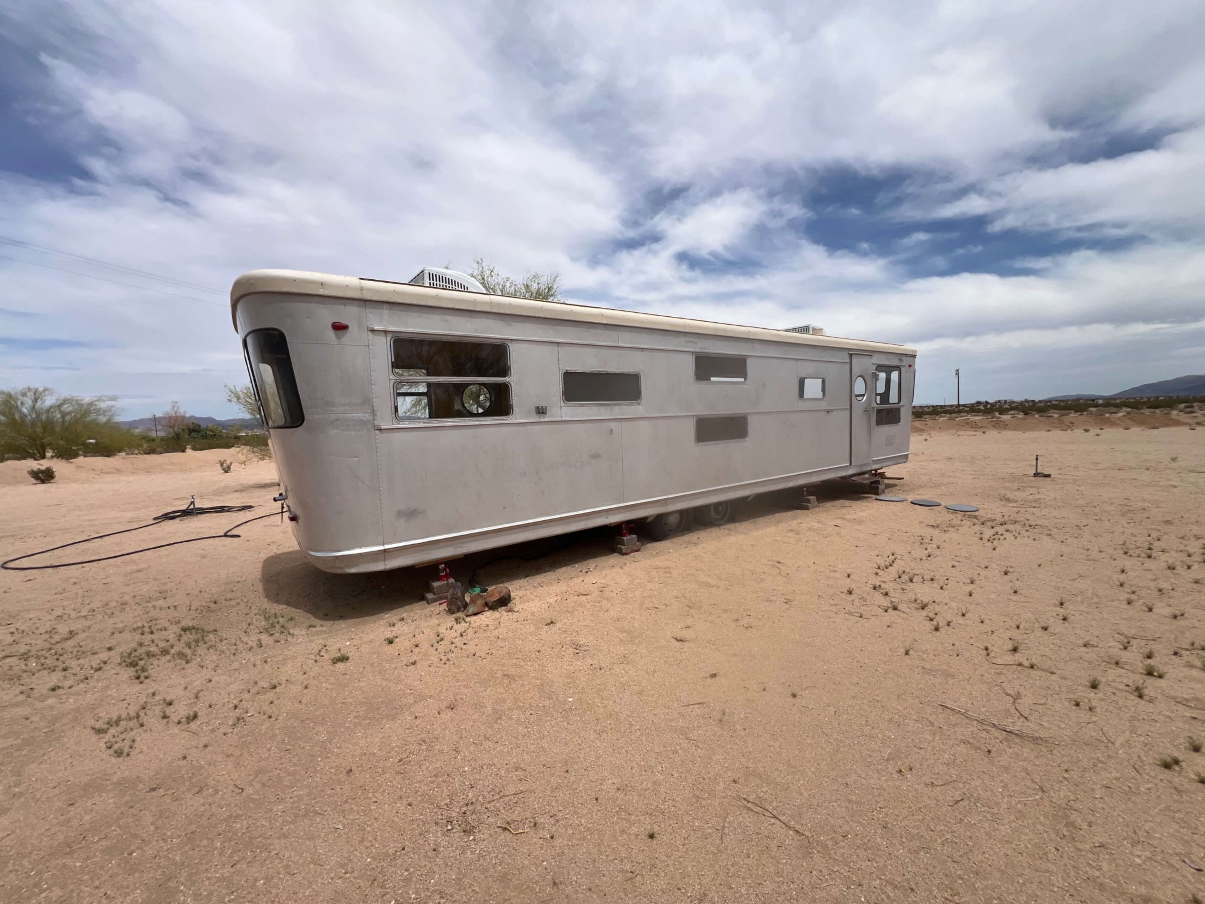 A vintage travel trailer is parked on dry, sandy terrain under a partly cloudy sky.