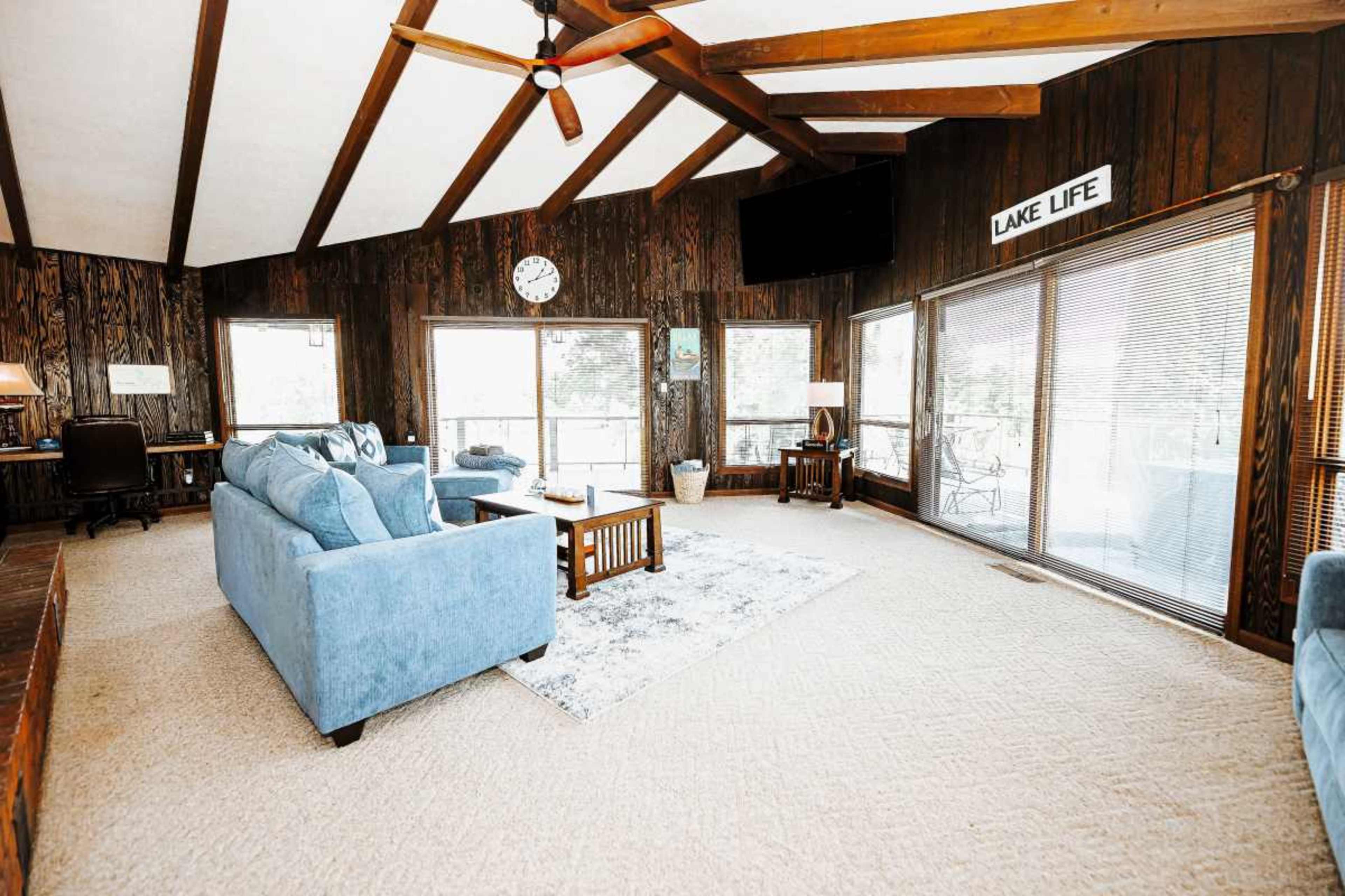 The living room features wooden walls, vaulted ceilings with exposed beams, and large windows that overlook a deck.