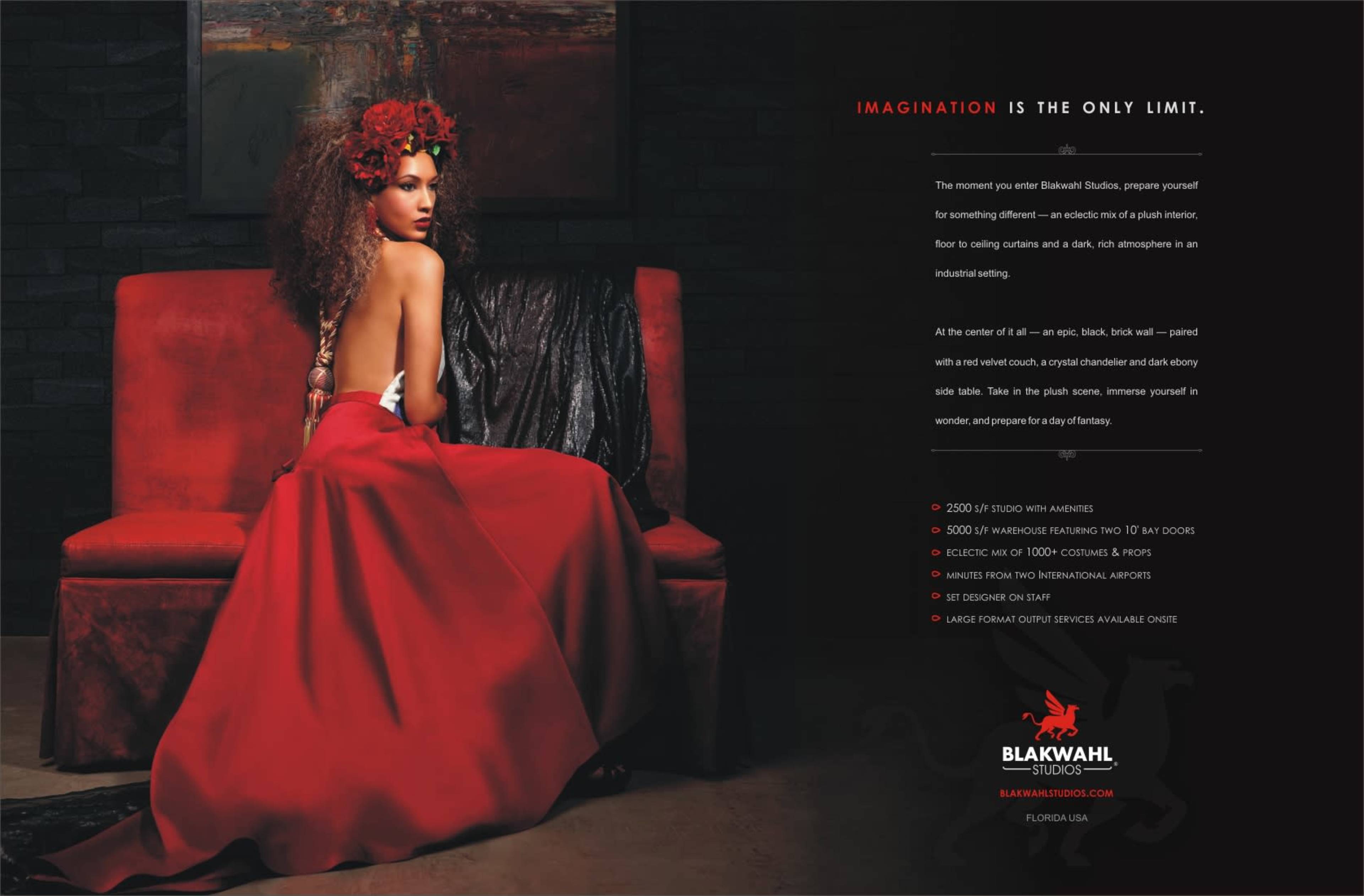 A woman sits on a red velvet couch, wearing a flowing red gown and a floral headdress, gazing over her shoulder.