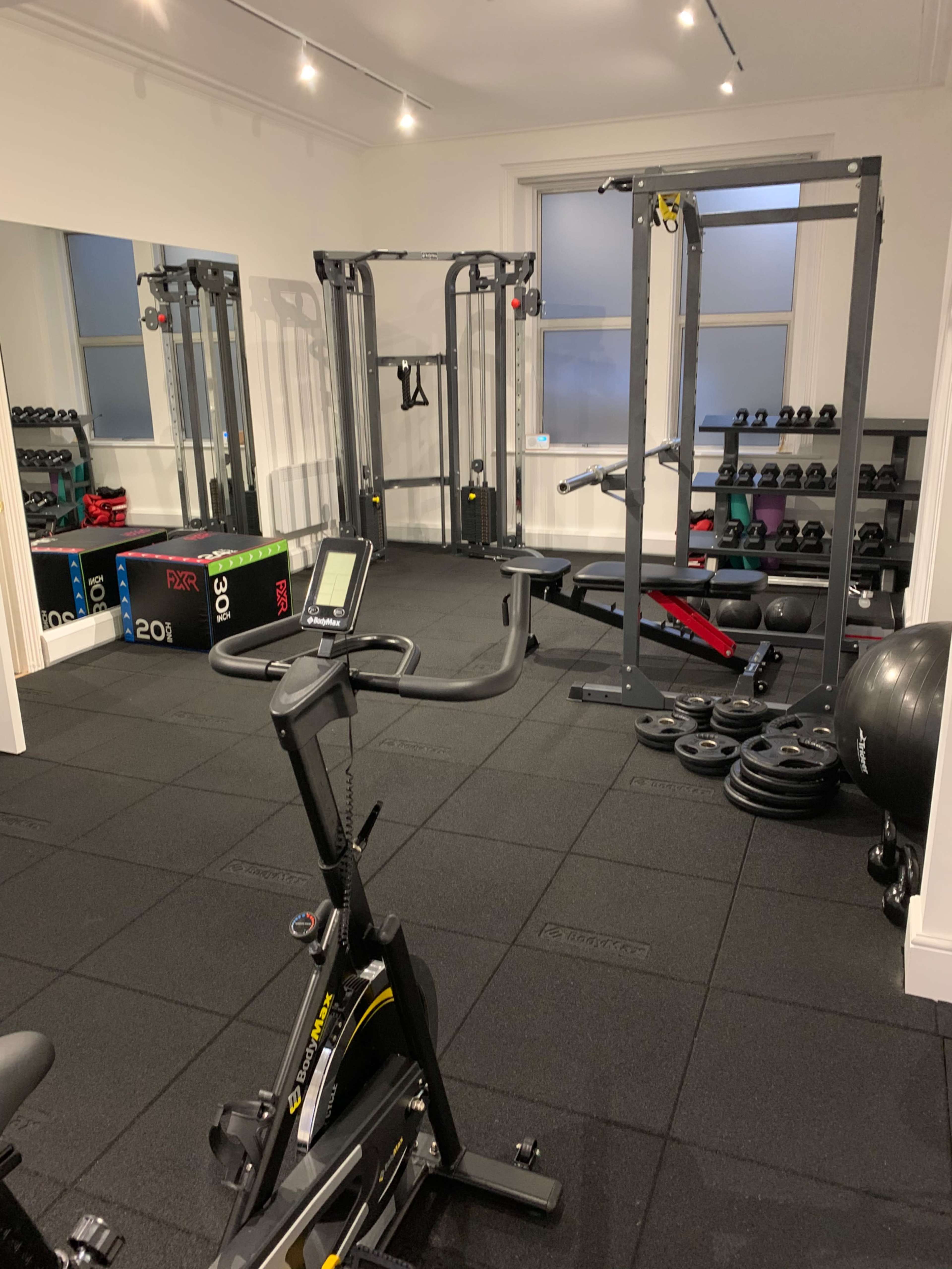 The image shows a home gym equipped with various exercise machines, weights, and fitness accessories arranged neatly in a well-lit room.