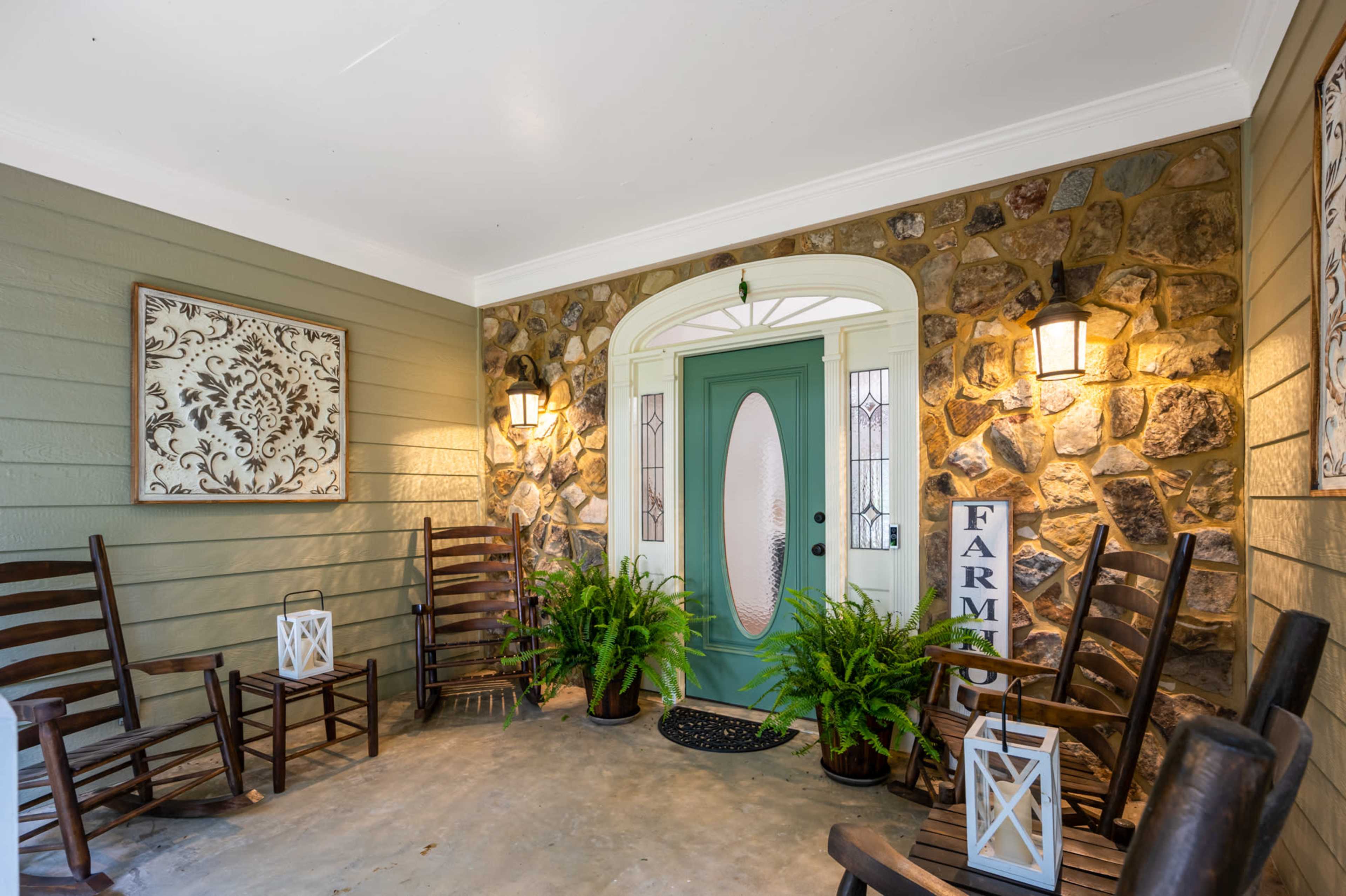 A porch featuring a stone wall, a teal front door, rocking chairs, and decorative lanterns.