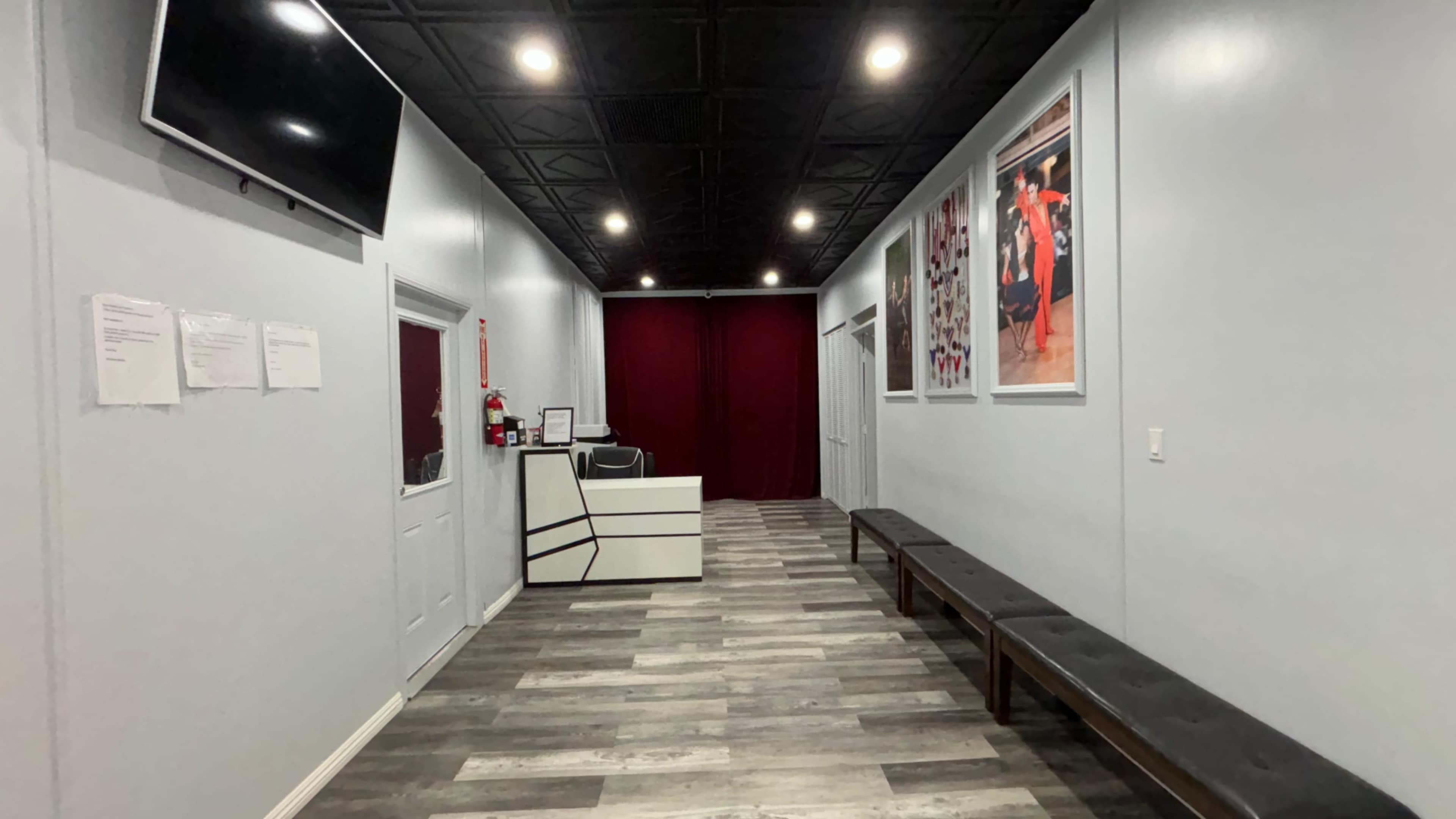 A long, narrow hallway with a reception area at the end, featuring gray walls, wooden flooring, and benches along the sides.