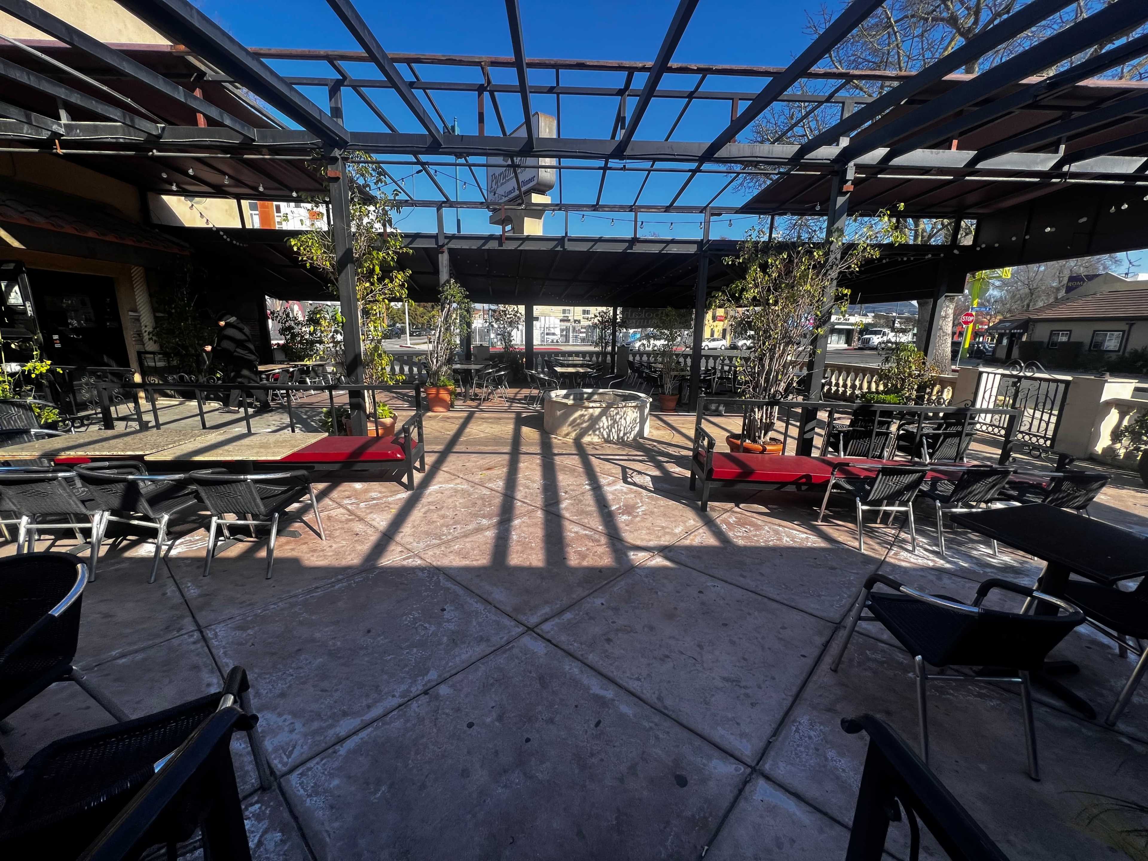 A patio area of a restaurant is set with metal chairs and tables, featuring a partially shaded seating arrangement.