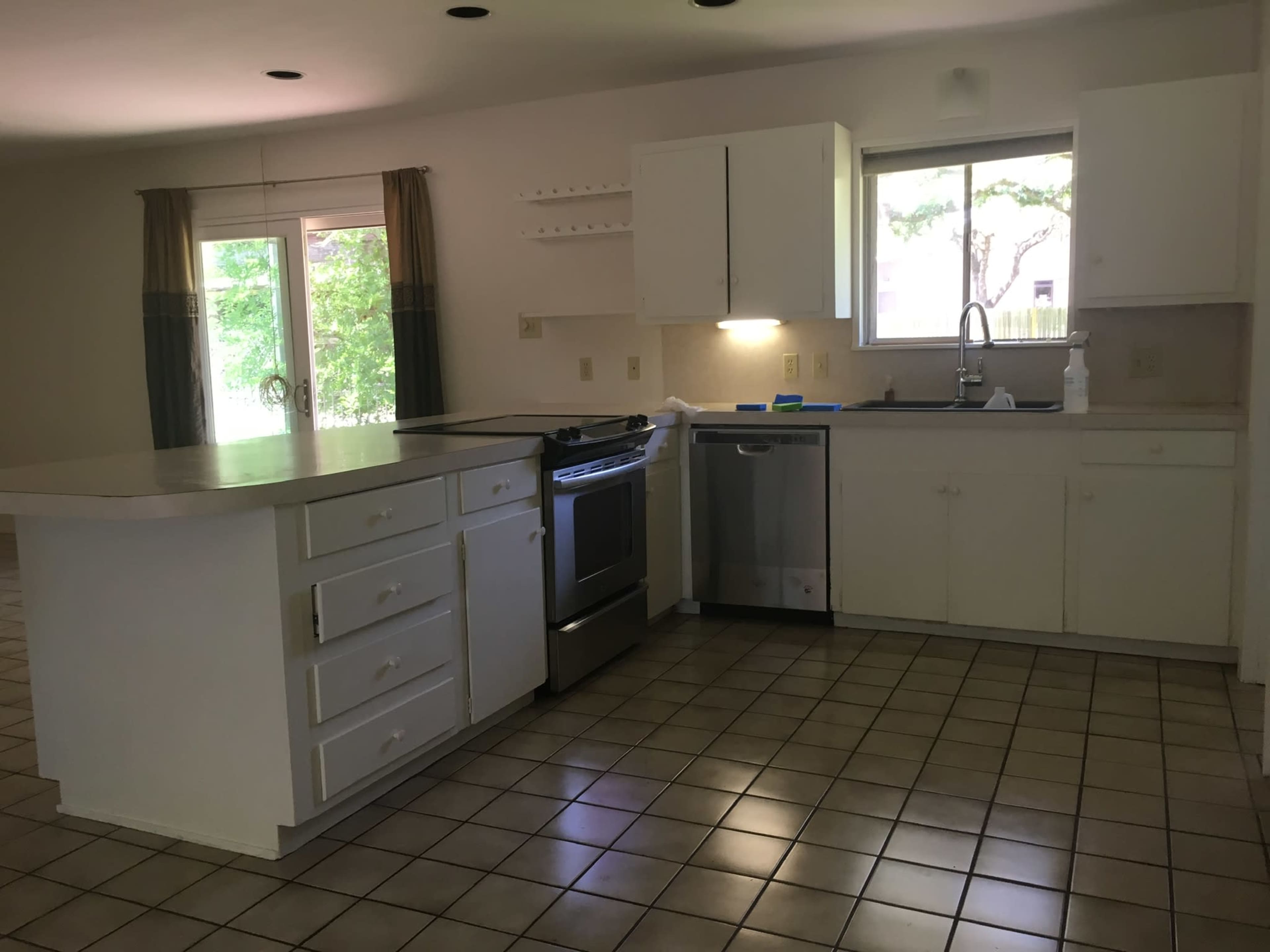 A kitchen with white cabinetry, a stainless steel stove, a dishwasher, and a window overlooking an outdoor area.