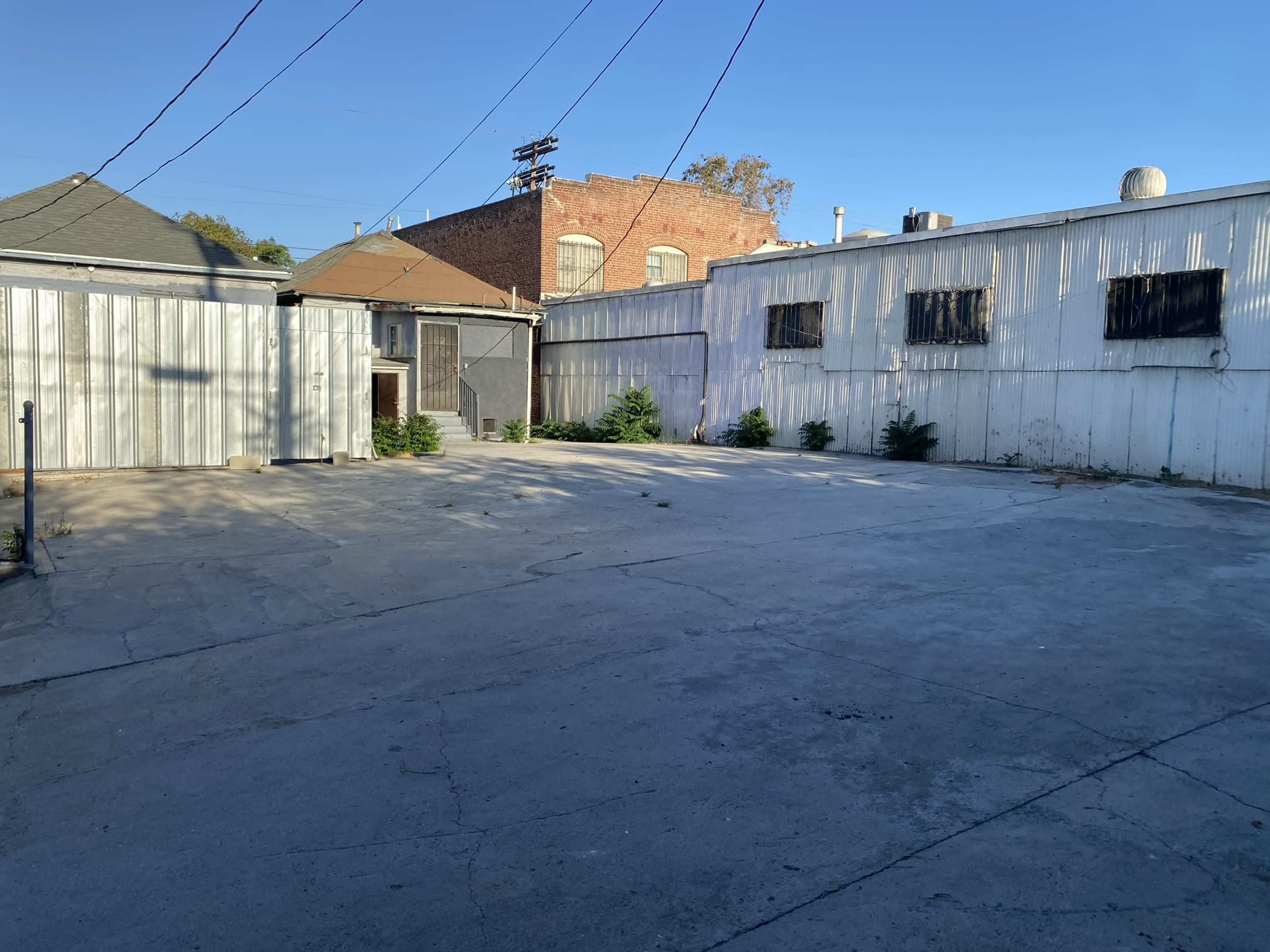 An empty concrete lot surrounded by metal and brick buildings under a clear blue sky.