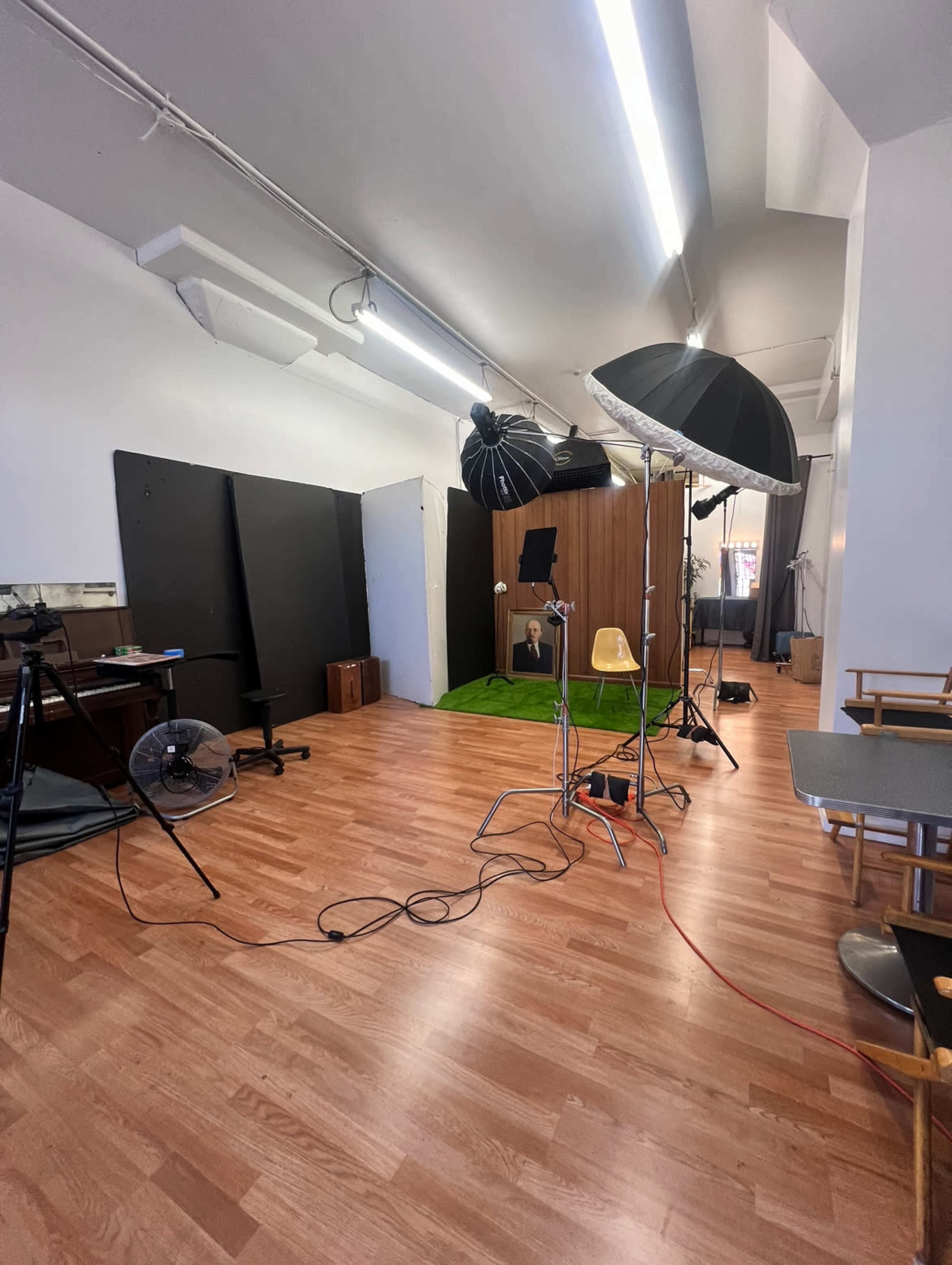The image shows a photography studio with lighting equipment, a green carpeted area, and various props arranged in the space.