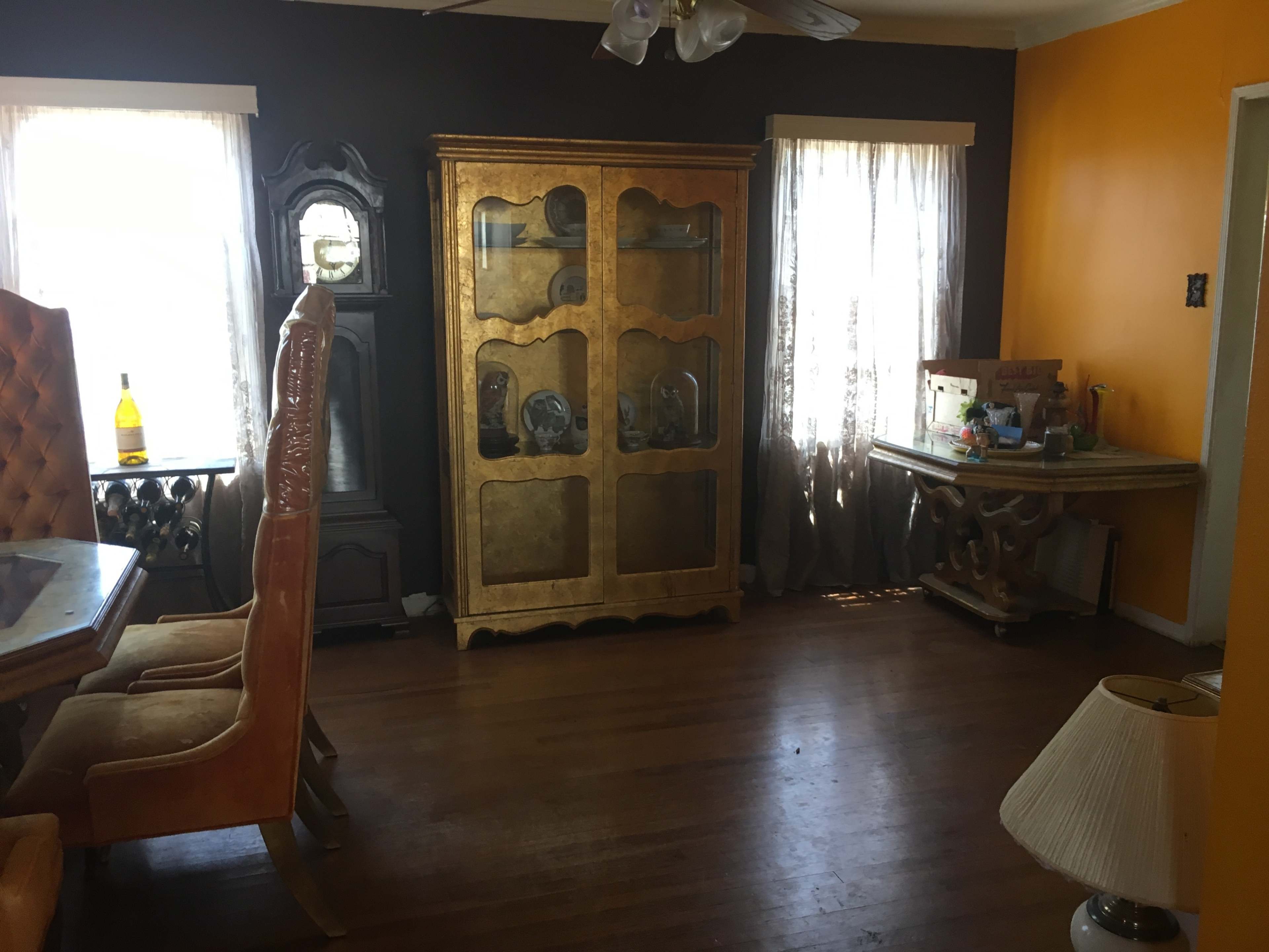 The room features a dining area with a wooden table and orange walls, complemented by a golden cabinet and a vintage clock.