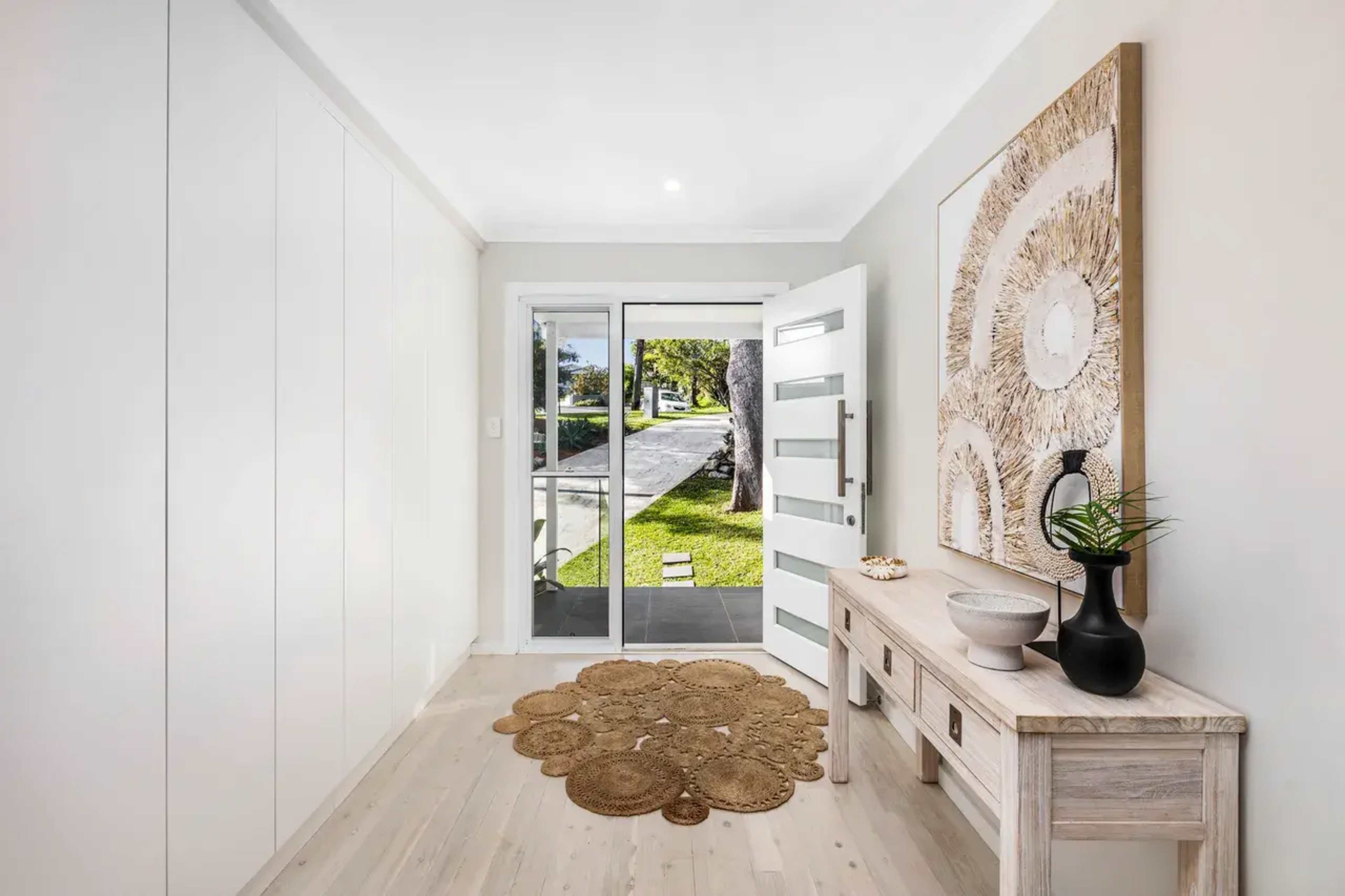 A modern entryway features a console table, a round rug, and a glass door leading to a view of the outside street.