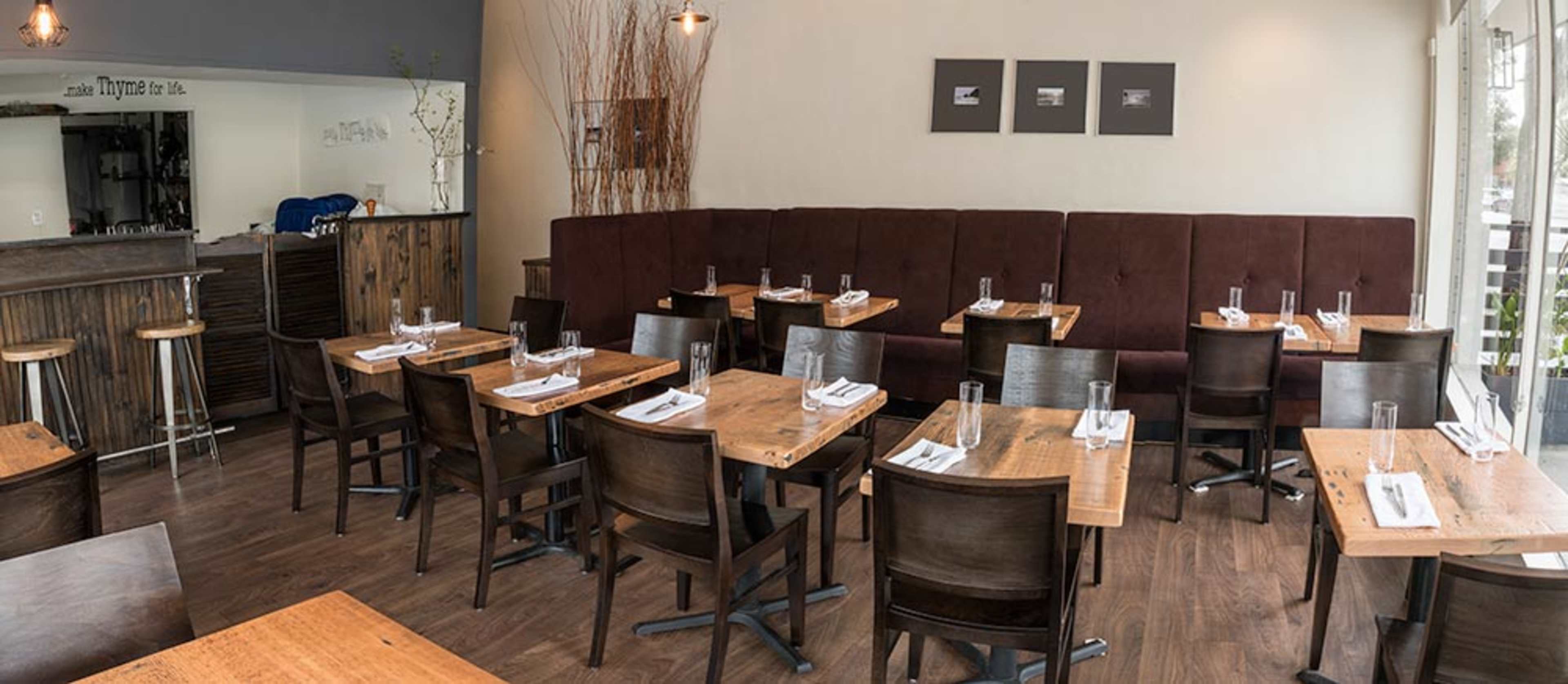 A modern restaurant interior featuring wooden tables and chairs arranged neatly, with a large upholstered booth along one wall.