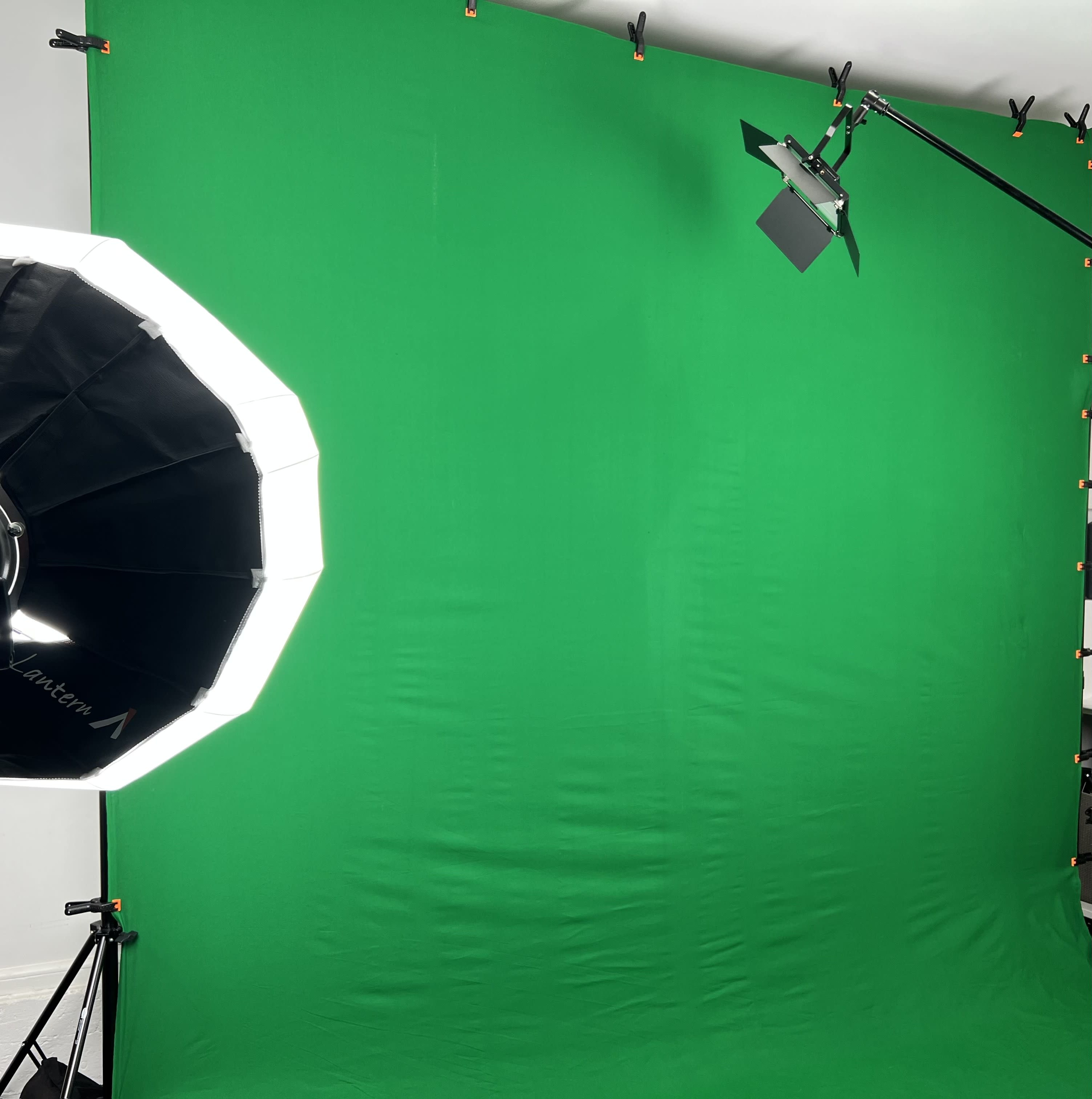 A green backdrop set up in a studio, accompanied by a lighting setup with a softbox and a spotlight.