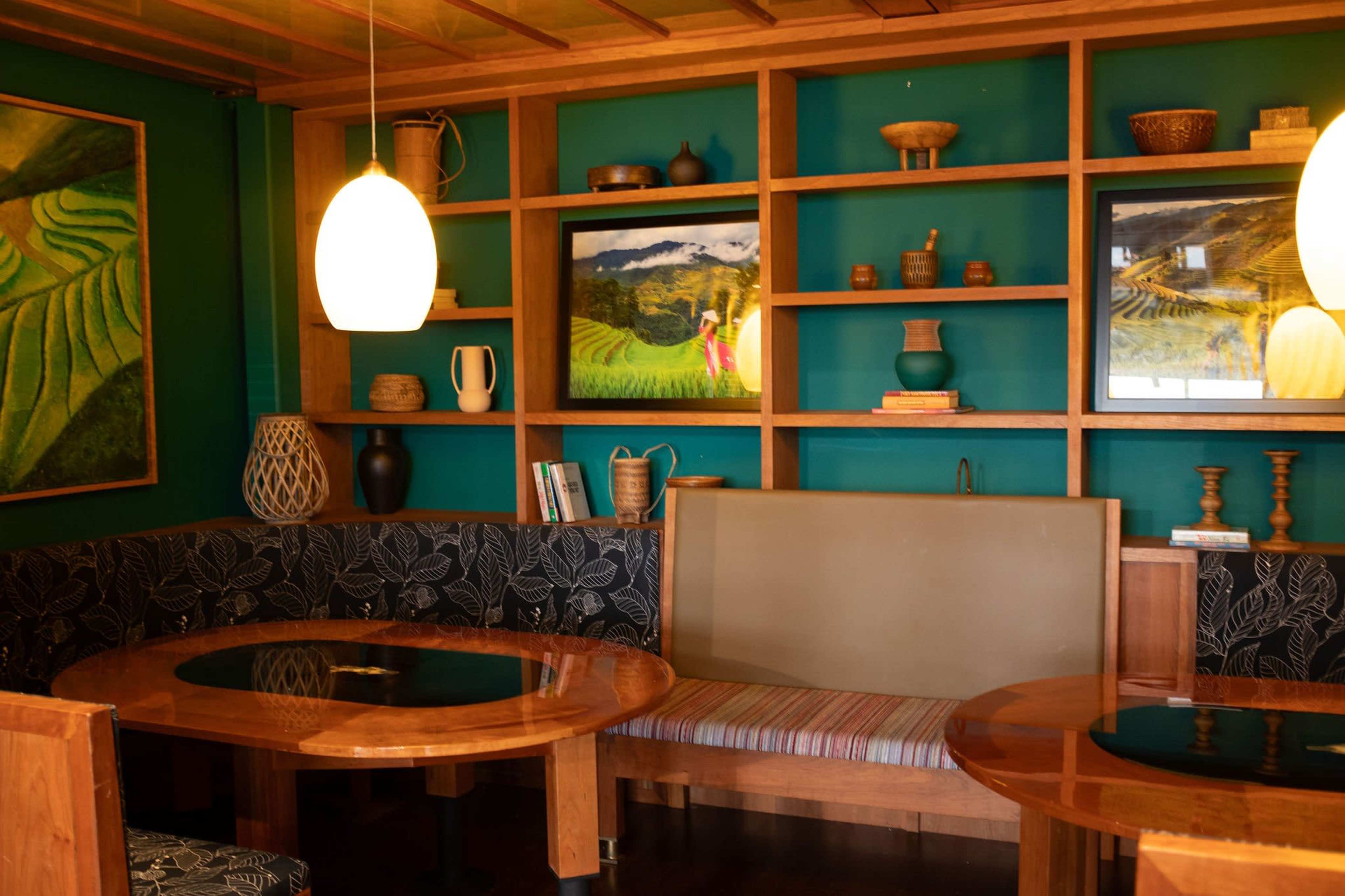 The image shows a cozy dining space with wooden furniture, green walls, and decorative shelves displaying various items and artwork.