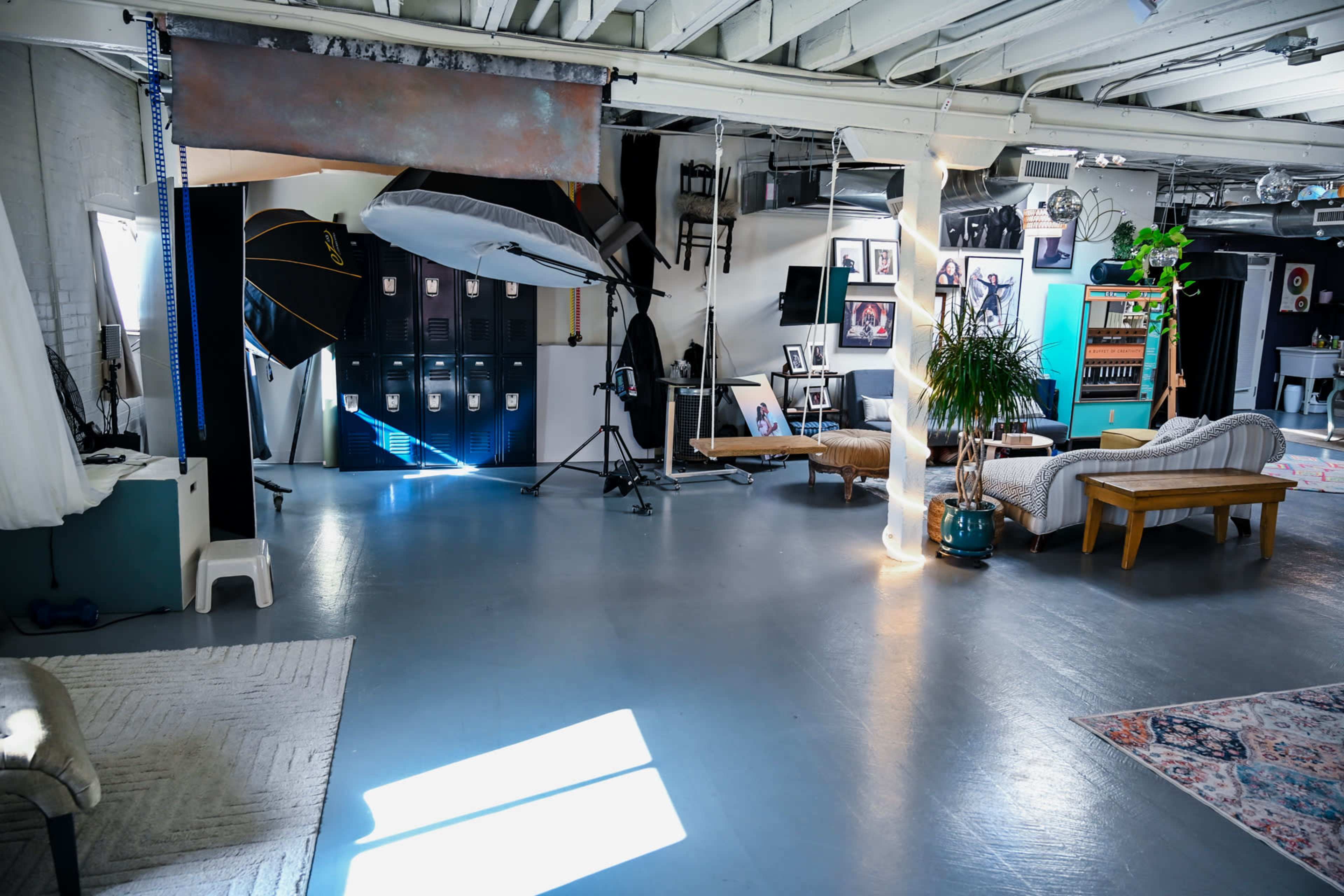 The image shows a spacious studio with various lighting equipment, lockers, and furniture arranged for creative use.