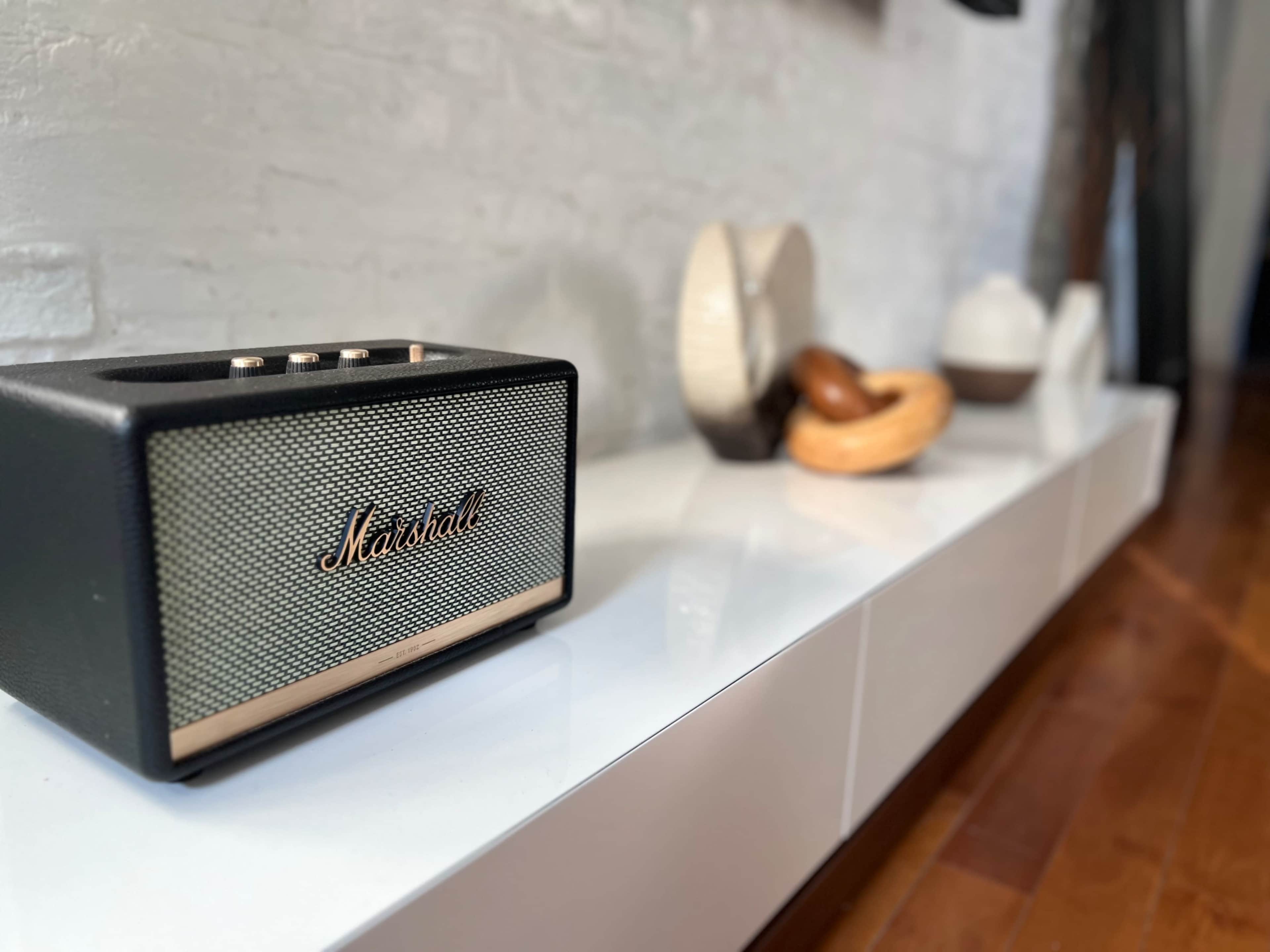 A black Marshall speaker sits on a glossy white shelf next to various decorative objects.