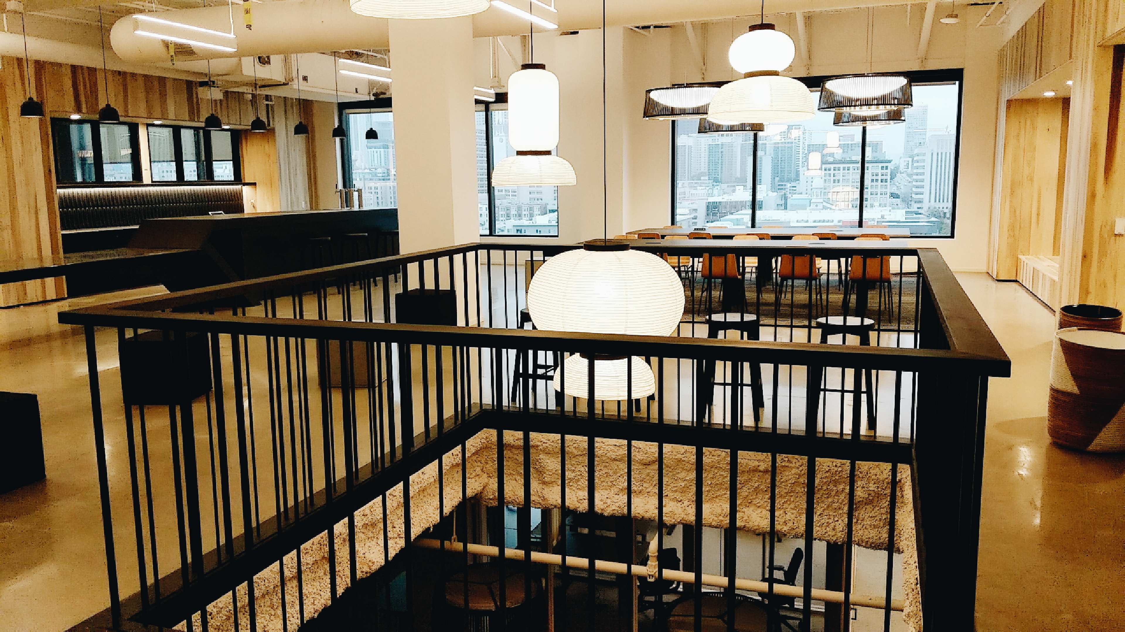 A modern office space with wooden accents, featuring a multi-level design, large windows, and various pendant lights hanging from the ceiling.