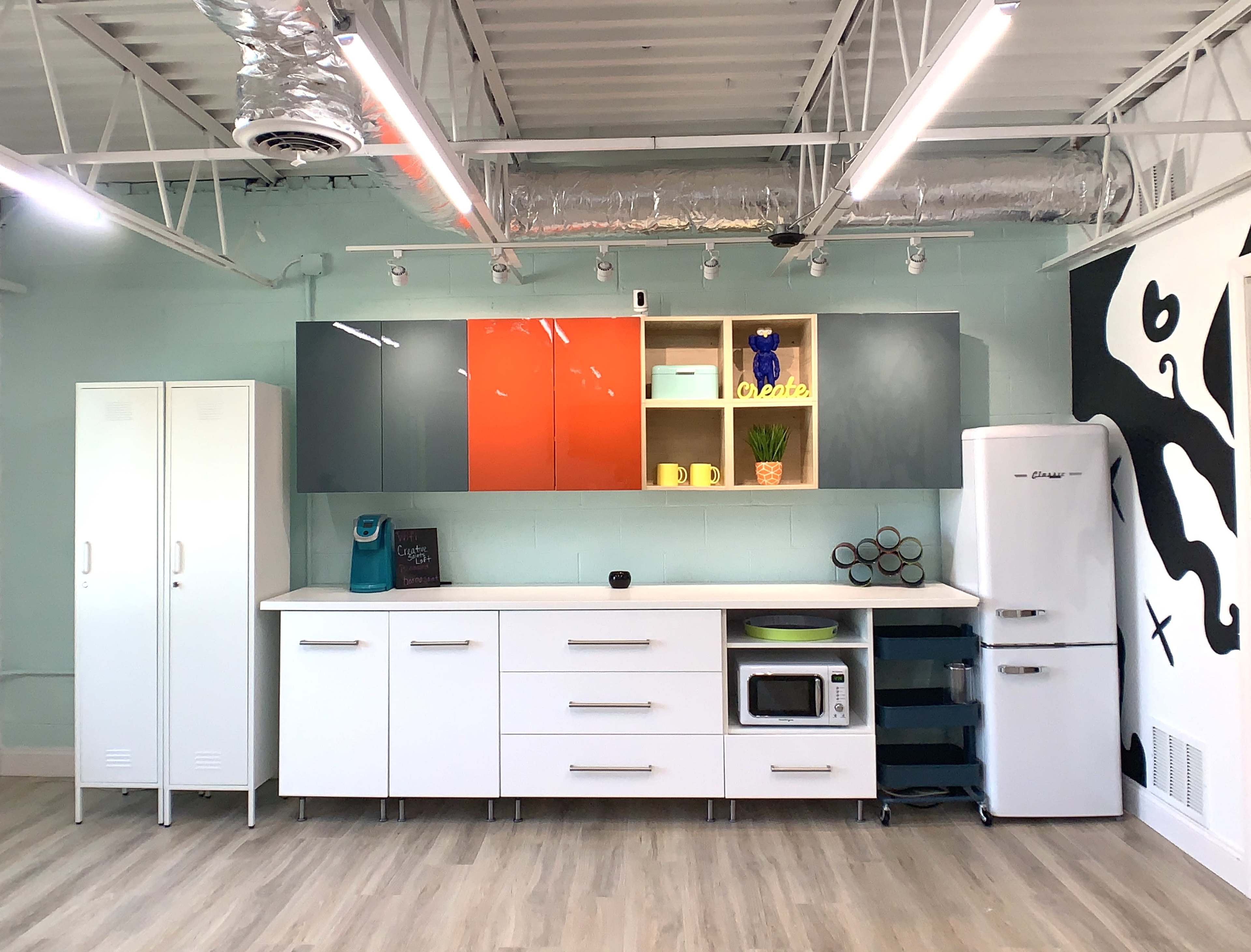 A modern kitchen setup with a white countertop, cabinets in various colors, and appliances including a microwave and refrigerator.