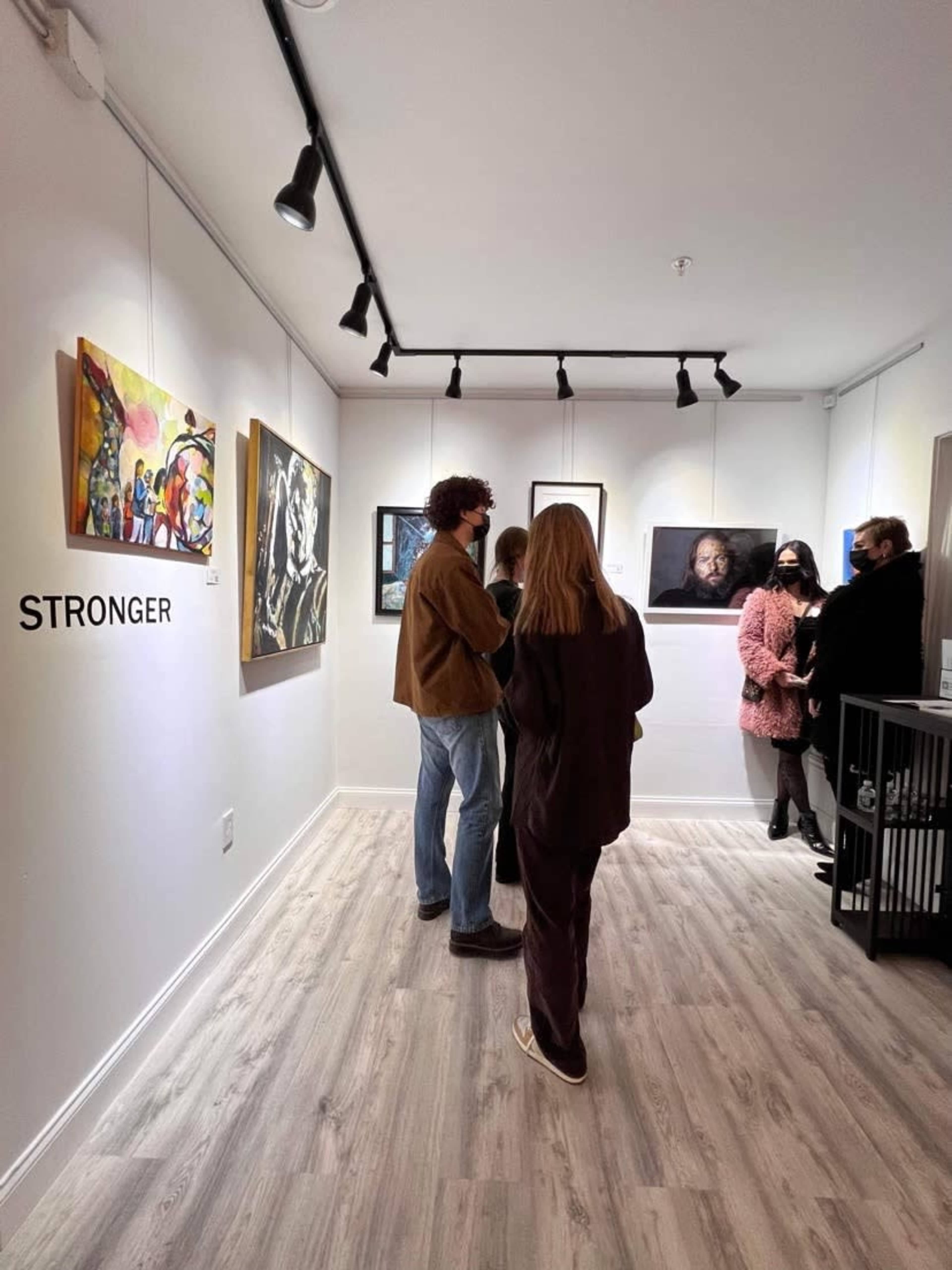 A group of people discusses artwork in a gallery with paintings displayed on the walls.