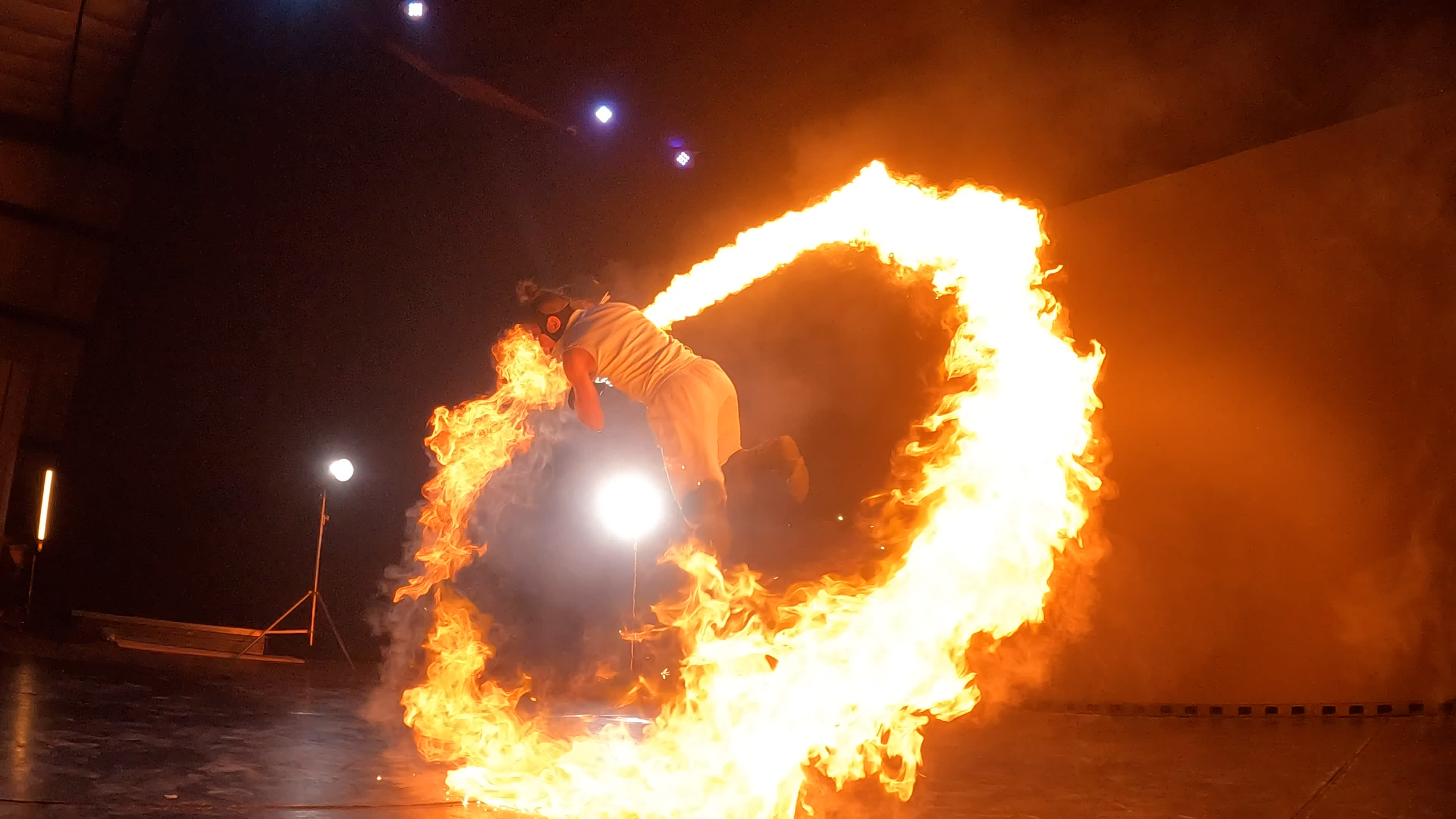 A performer leaps through a ring of fire on stage illuminated by spotlights.