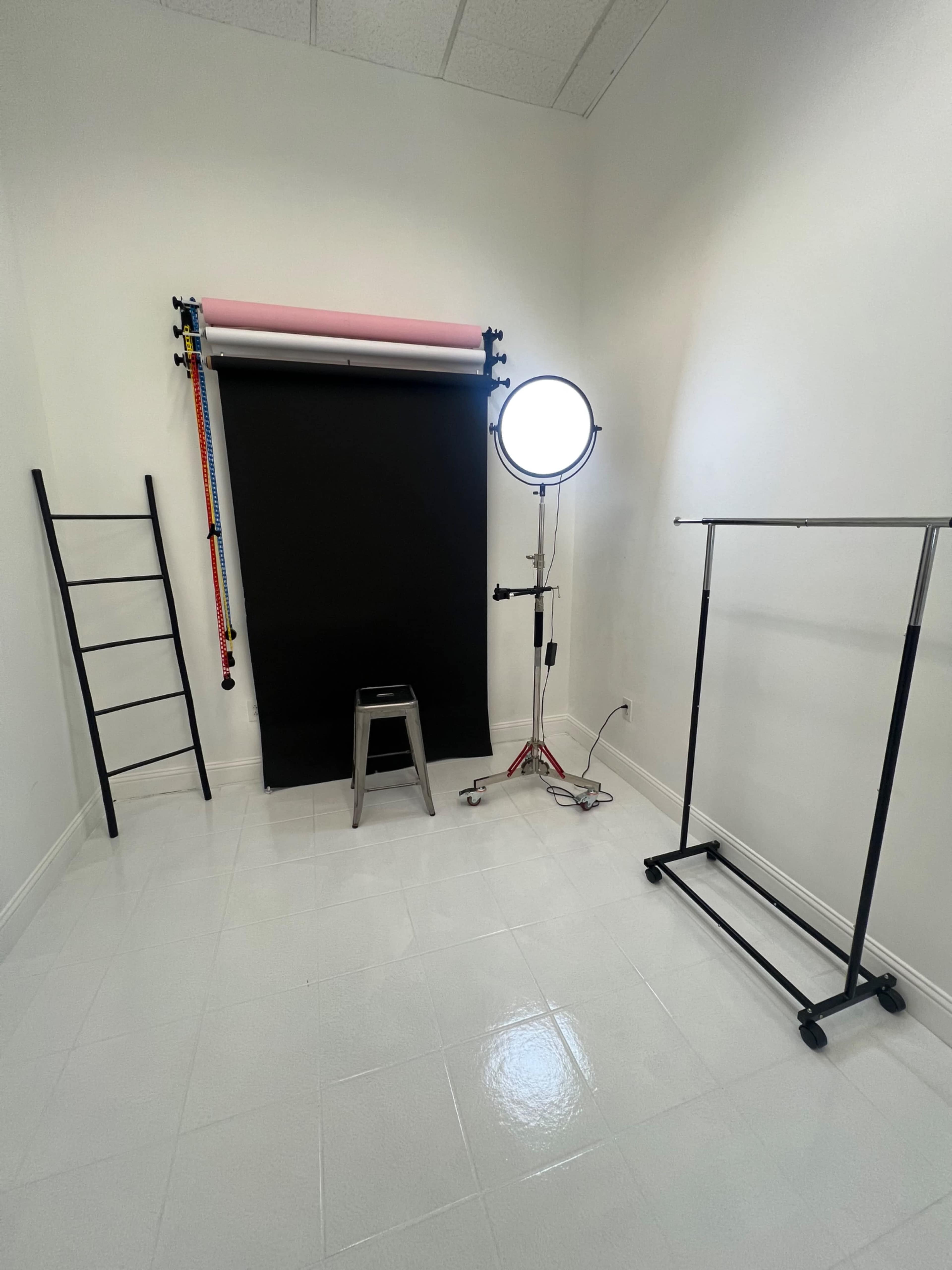 A photography studio features a black backdrop, a lighting setup, and a clothes rack on a polished white floor.