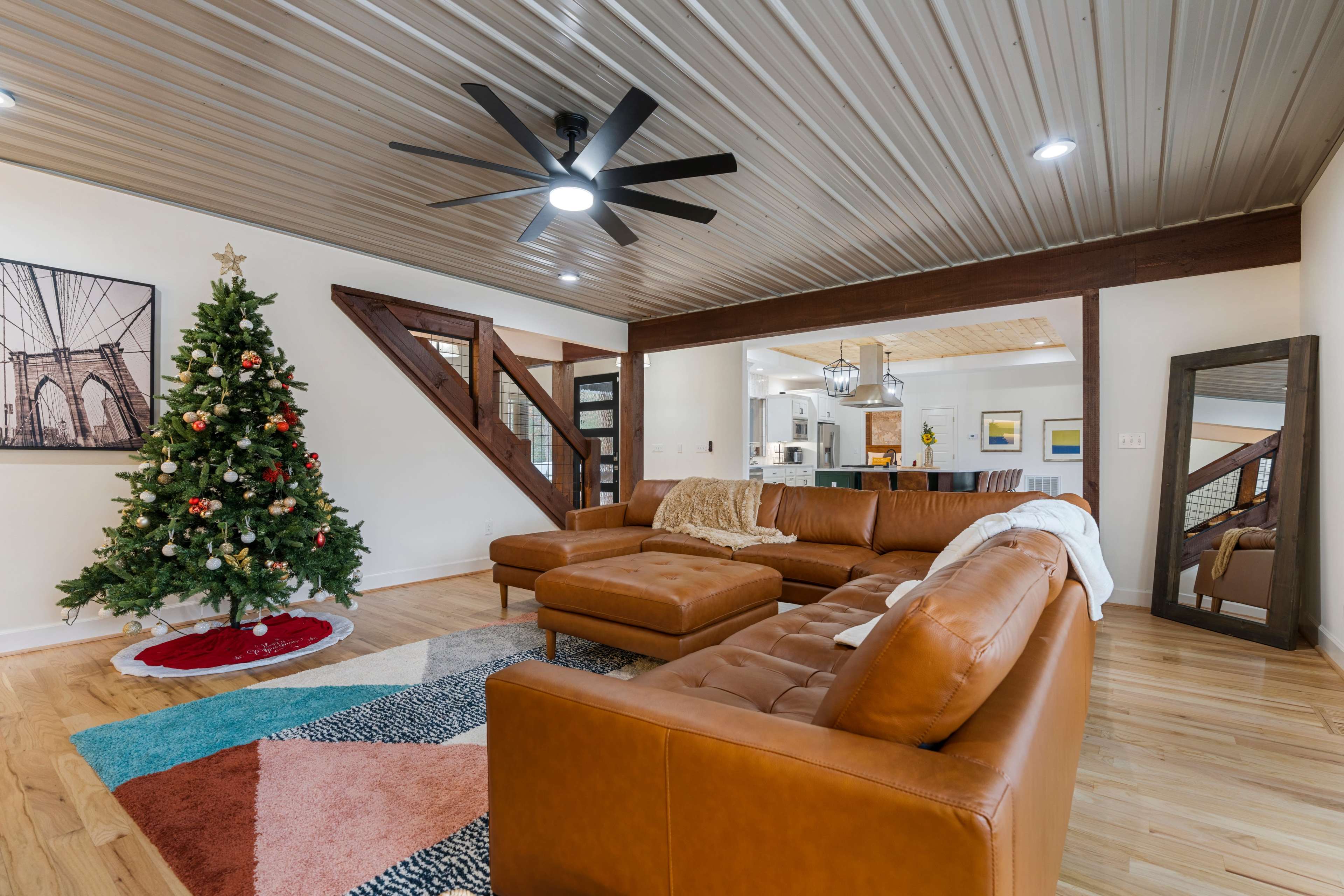 The living room features a brown leather sectional sofa, a Christmas tree, and a view of an open kitchen area in the background.