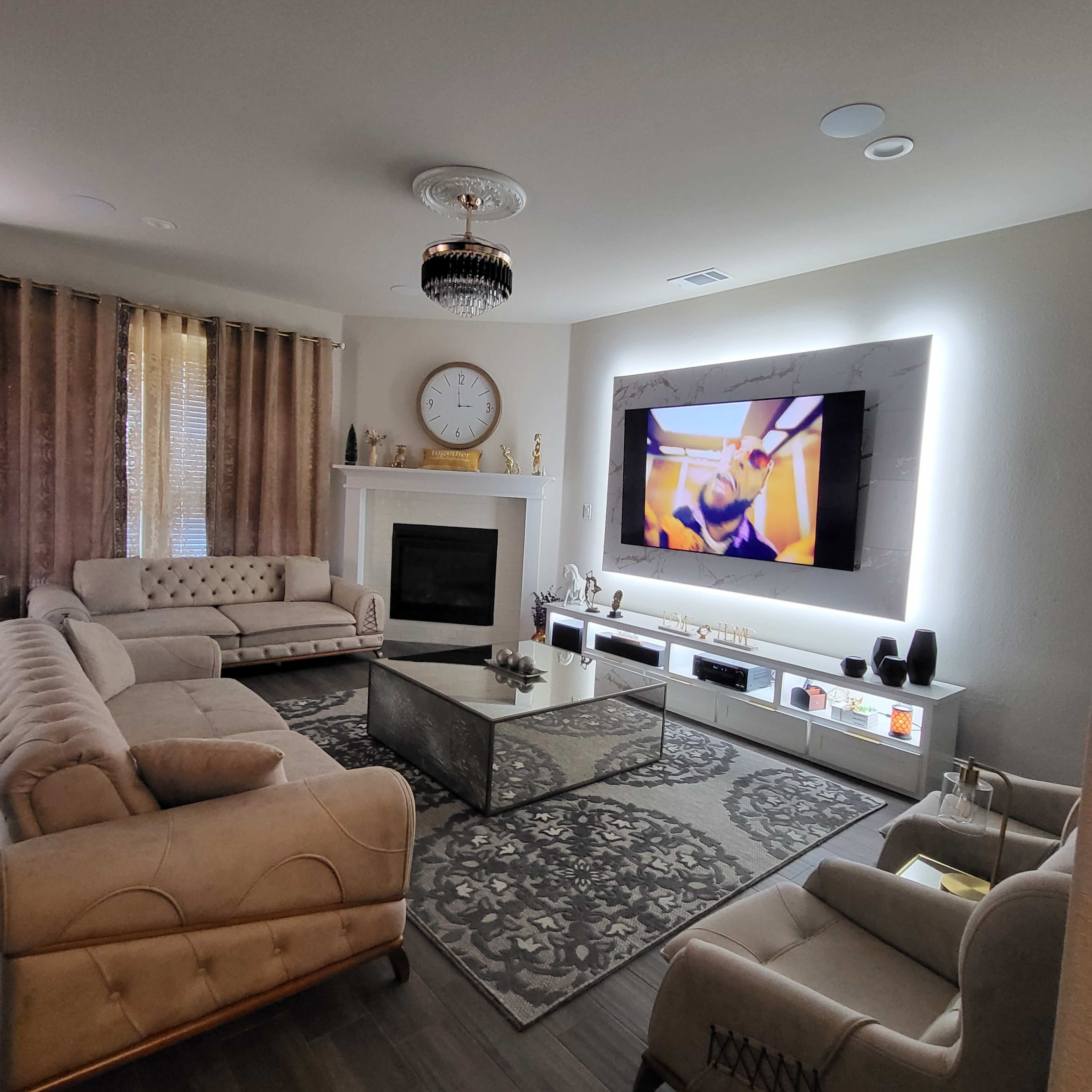 A modern living room featuring a fireplace, a large television mounted on the wall, a coffee table, and two sofas arranged around a rug.