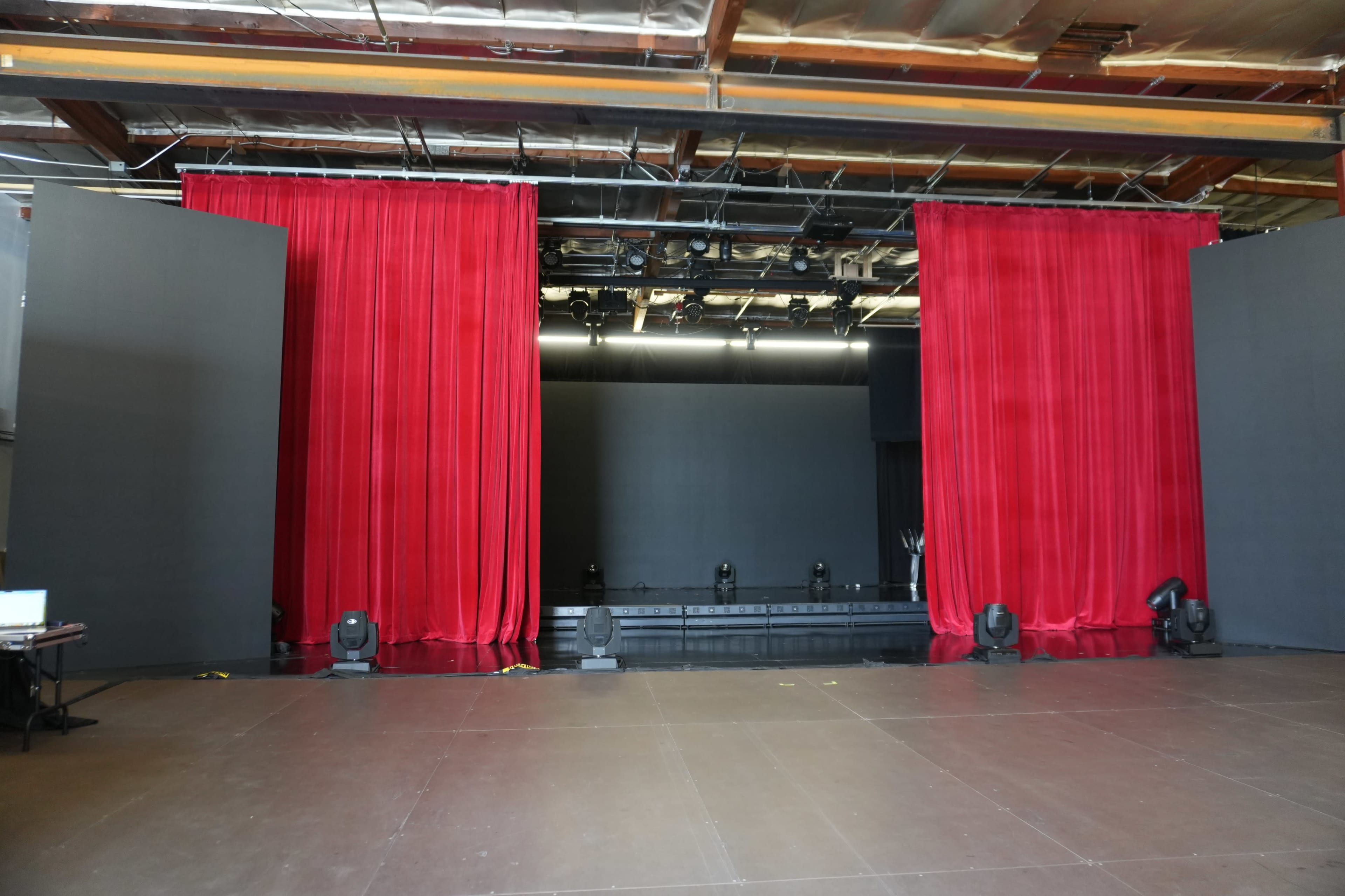 A stage is set with red curtains on either side and a dark backdrop, illuminated by stage lights.