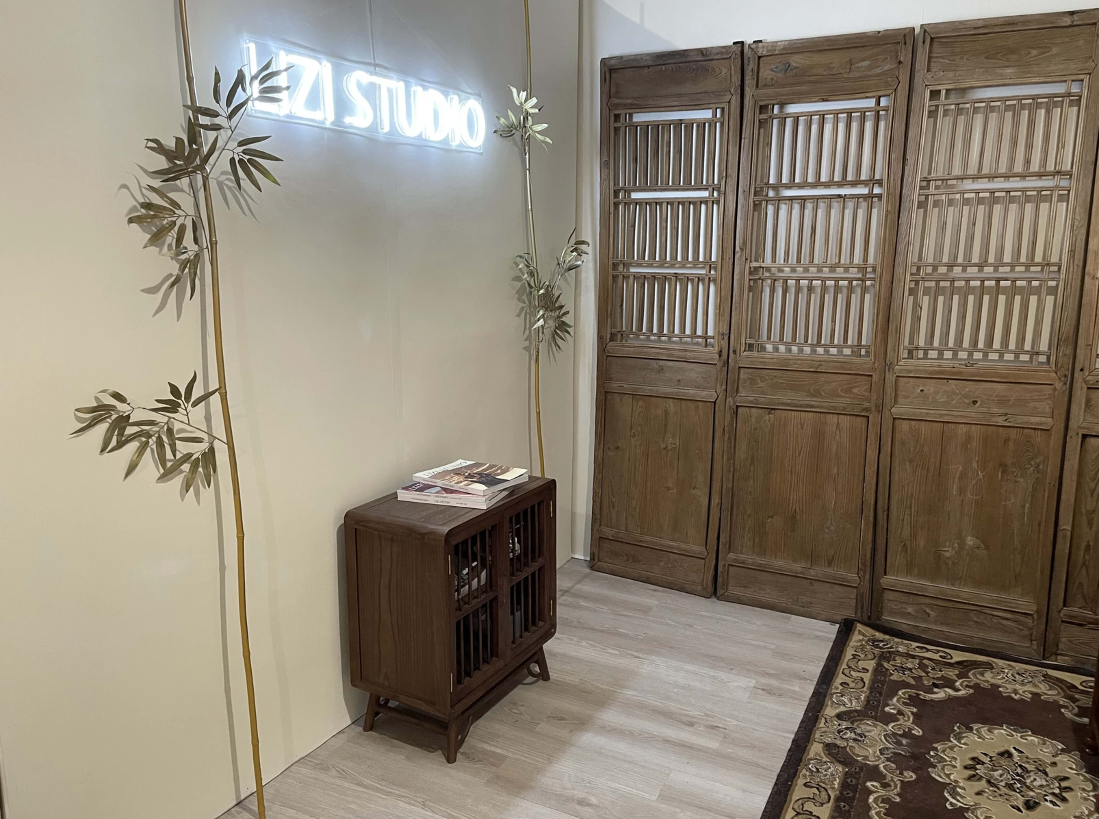A minimalist room with a "VEZI STUDIO" neon sign, a wooden cabinet, and wooden folding room dividers against a light wall.
