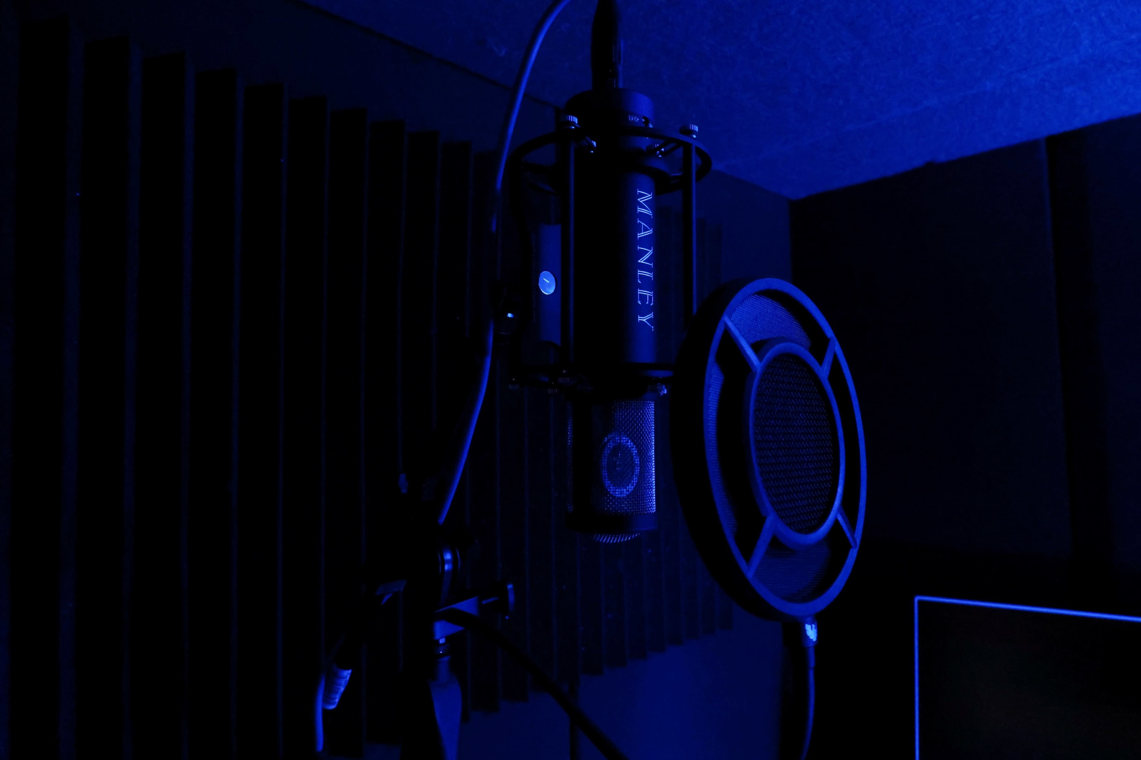 A high-quality microphone is mounted on a stand in a dimly lit studio with blue lighting and acoustic panels in the background.