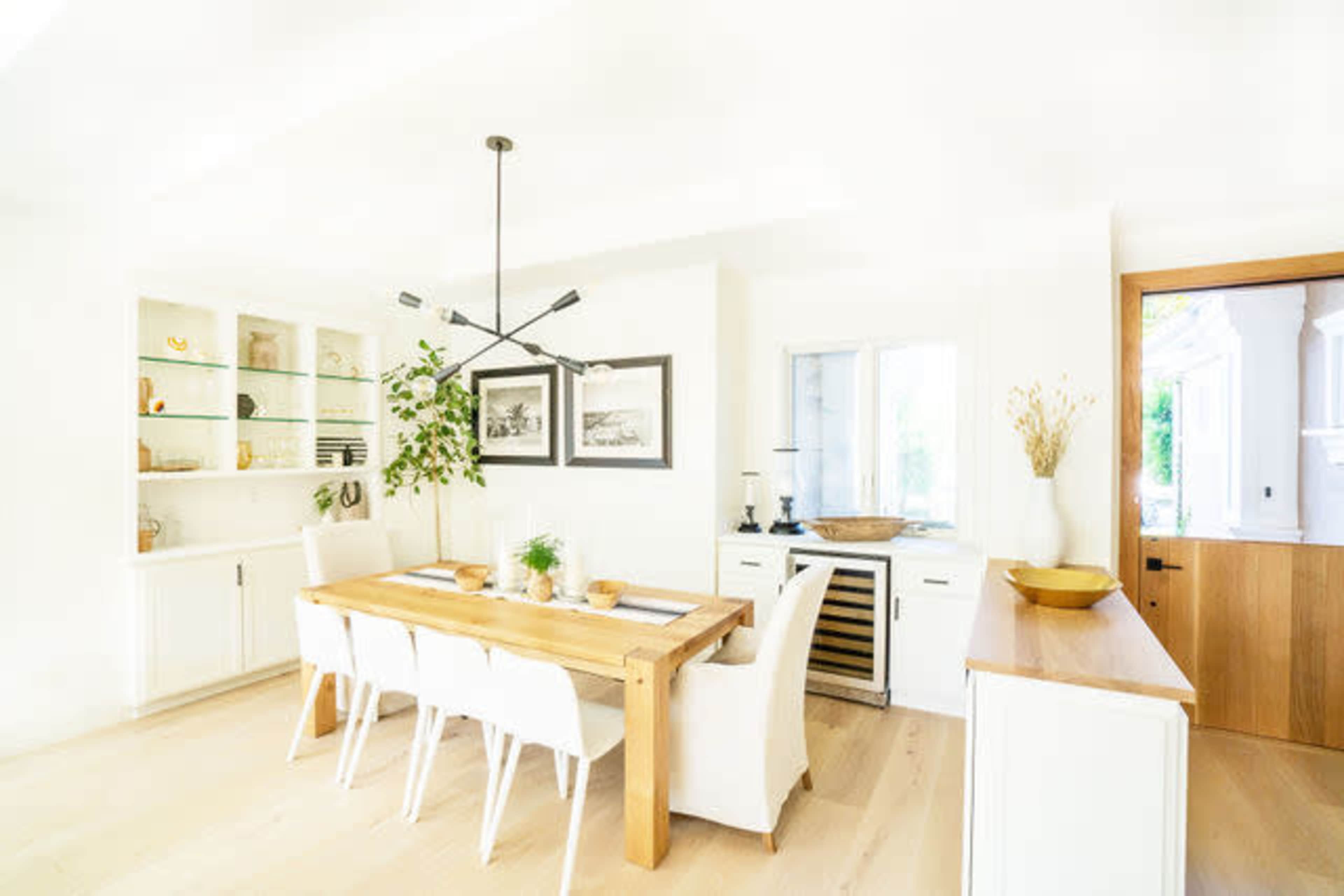 A bright dining area with a wooden table surrounded by white chairs, a built-in shelf displaying decorative items, and a door leading outside.