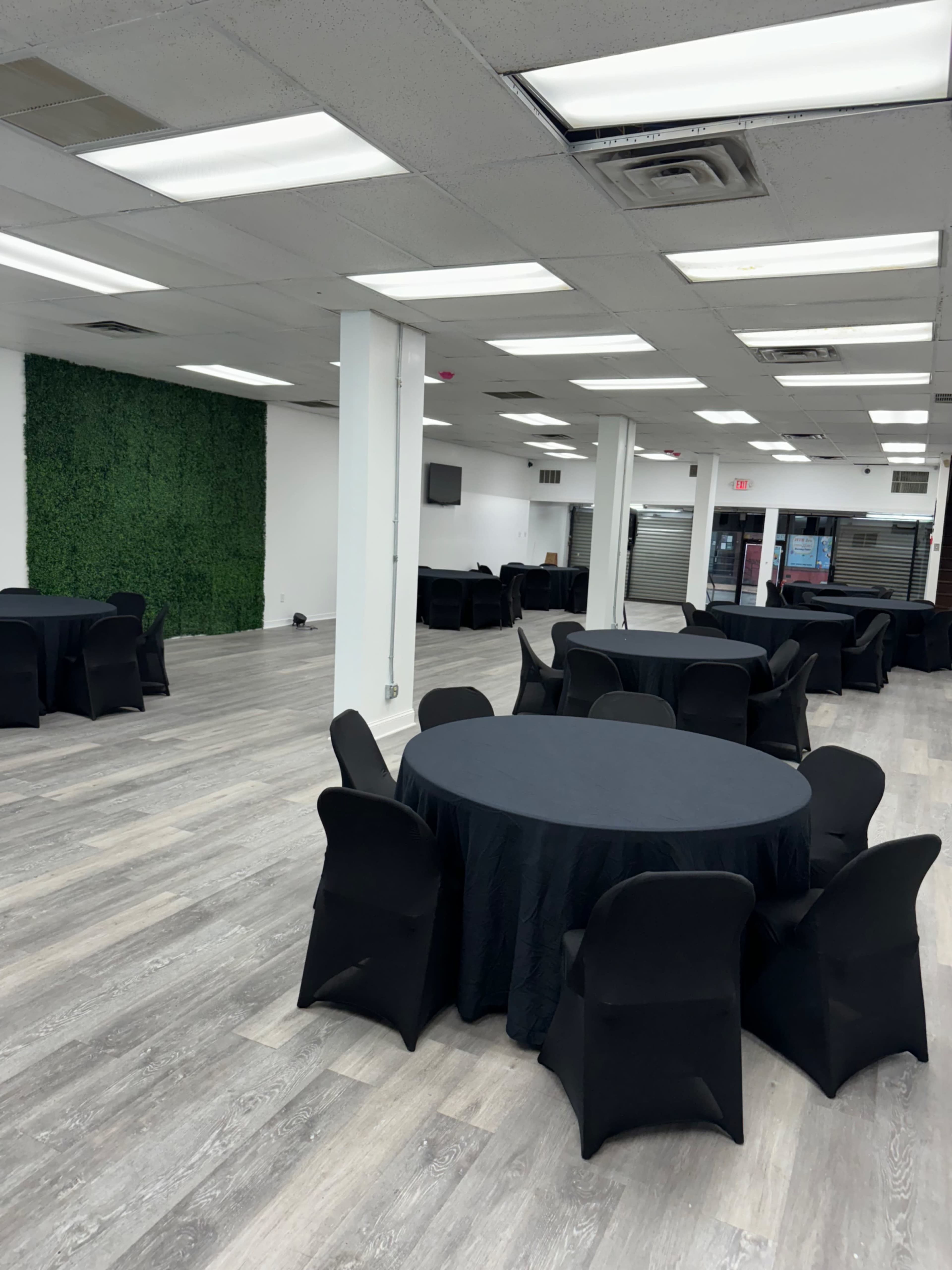 A spacious event room with several round tables covered in black tablecloths and a decorative green wall in the background.