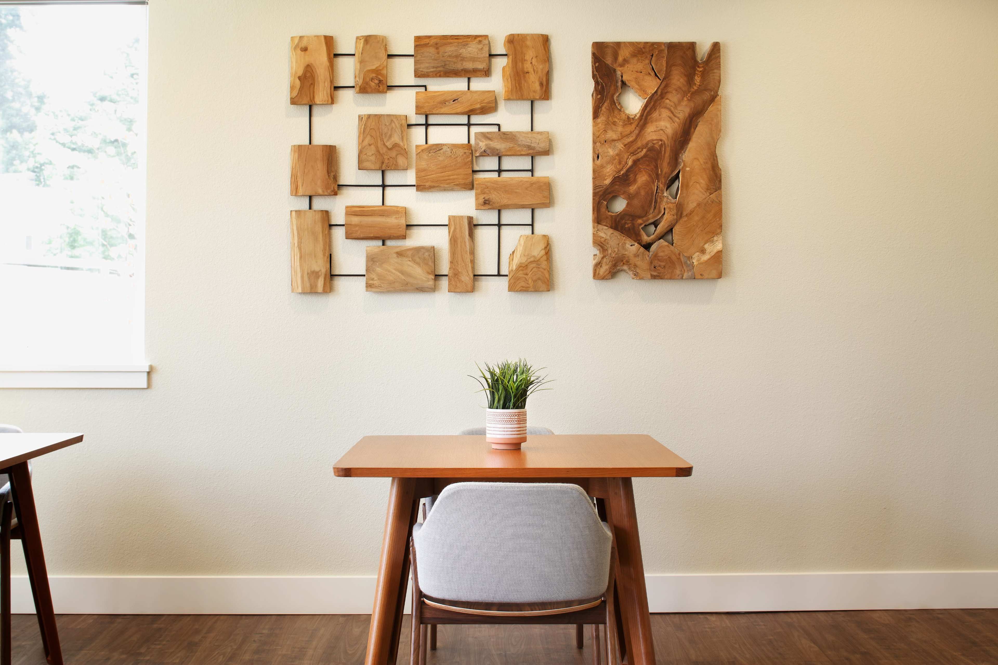 A minimalist dining area with wooden tables, one set with a small potted plant, and a wall featuring contemporary wood art pieces.