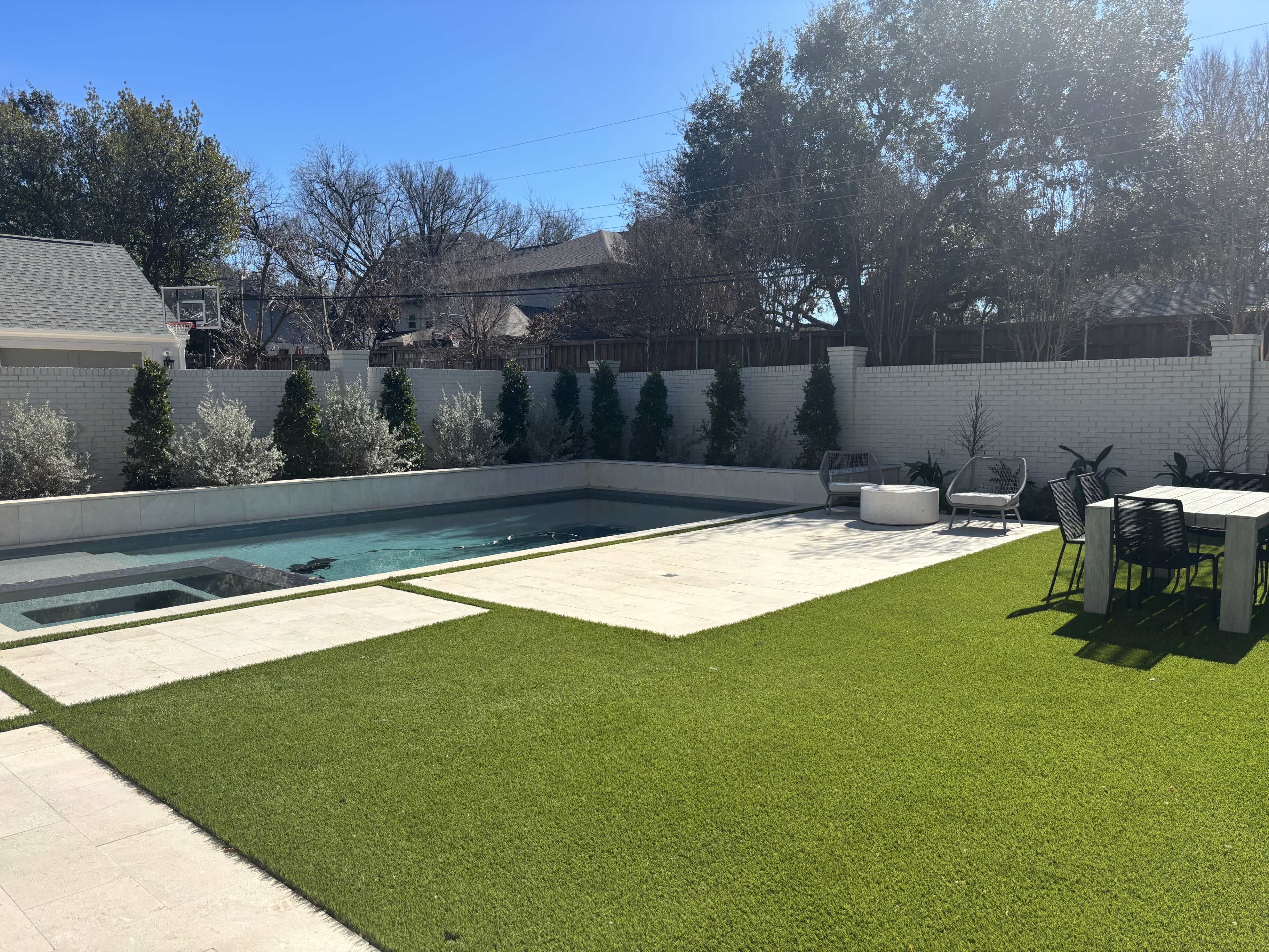 The image shows a backyard with a pool, a patio area with seating, and landscaped greenery.