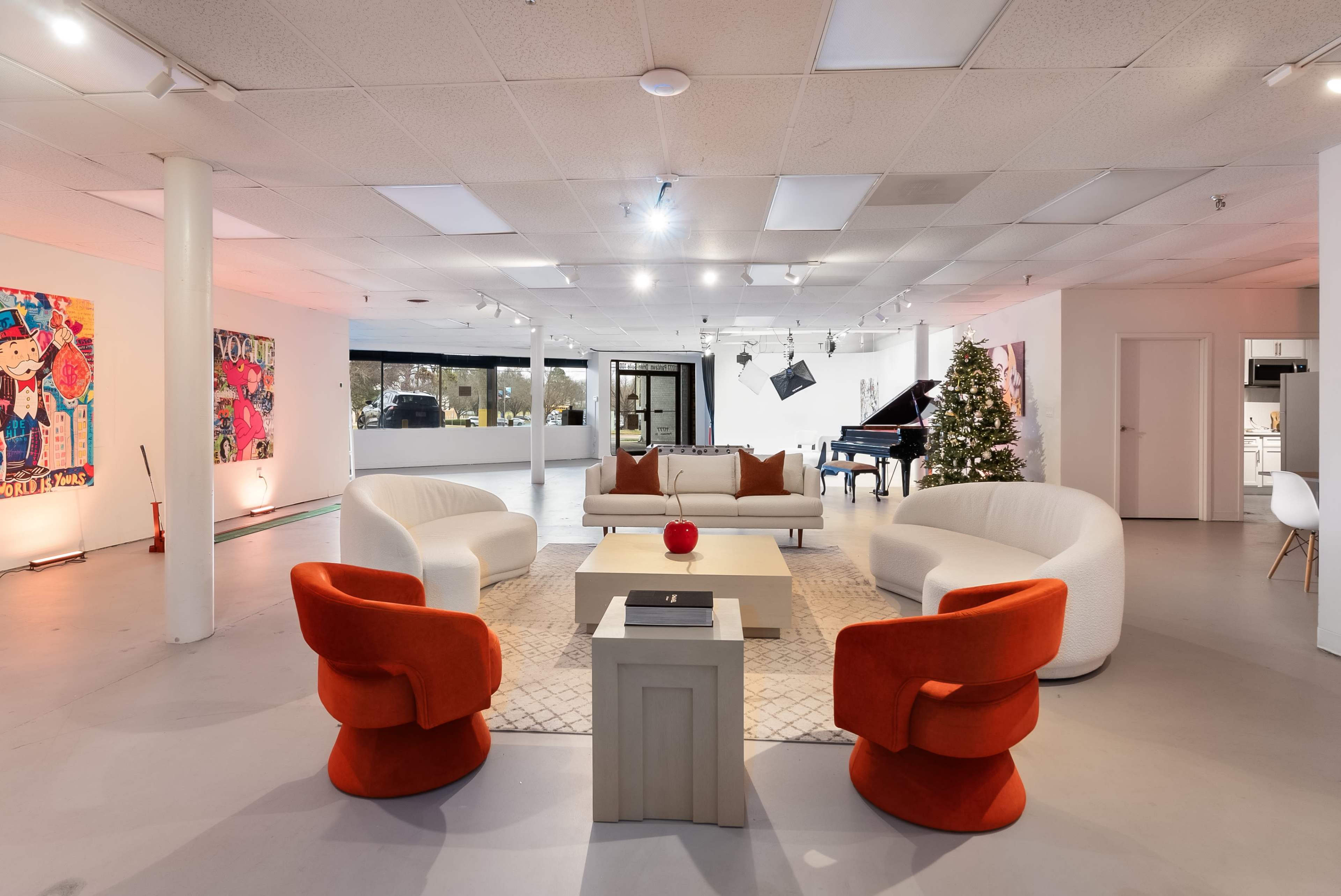 A spacious gallery-like interior features modern furniture, a grand piano, and art on the walls, with a Christmas tree in the corner.