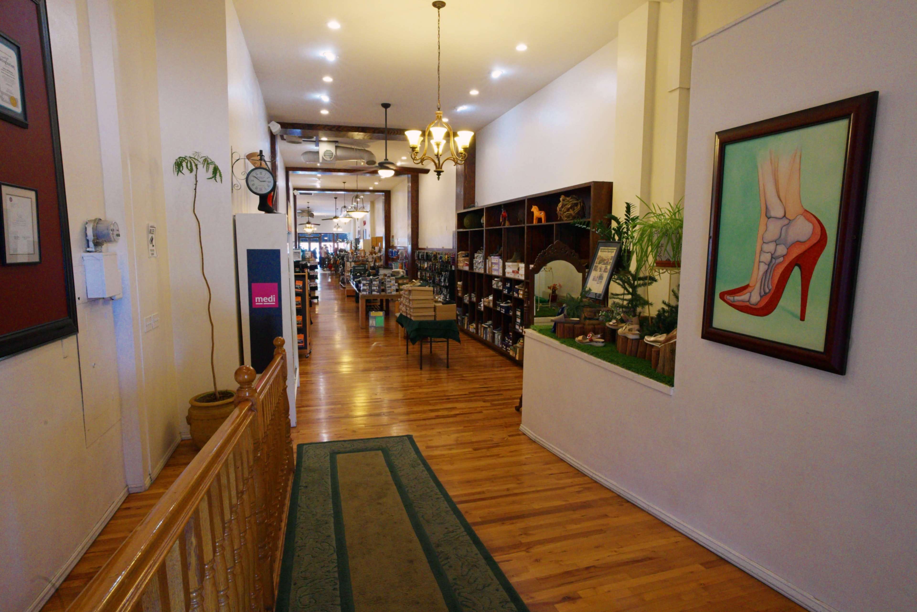 The image shows a long corridor of a retail space with wooden flooring and various displayed products along the sides, illuminated by ceiling lights.