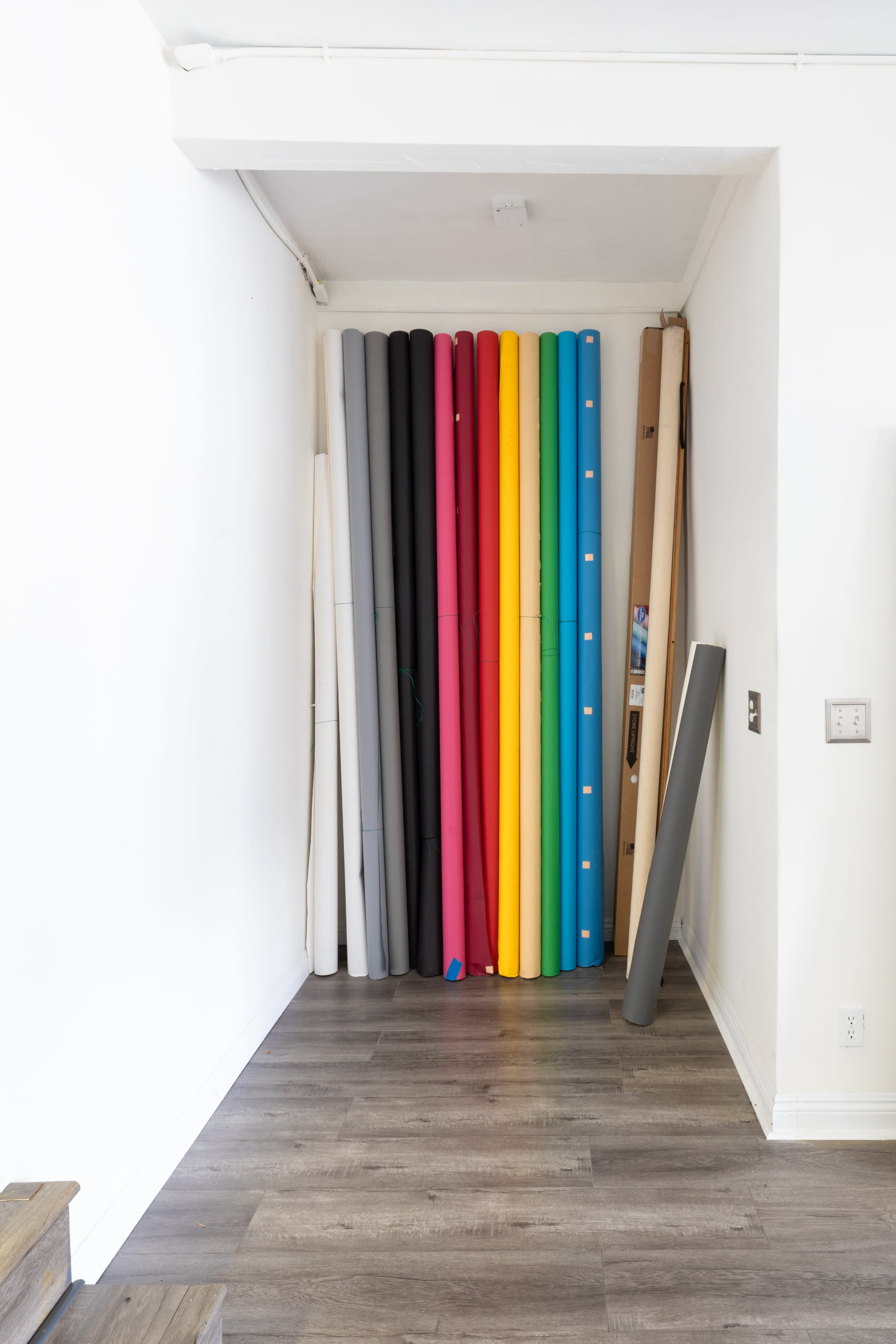 A narrow hallway with a collection of rolled materials in various colors stacked against a white wall.