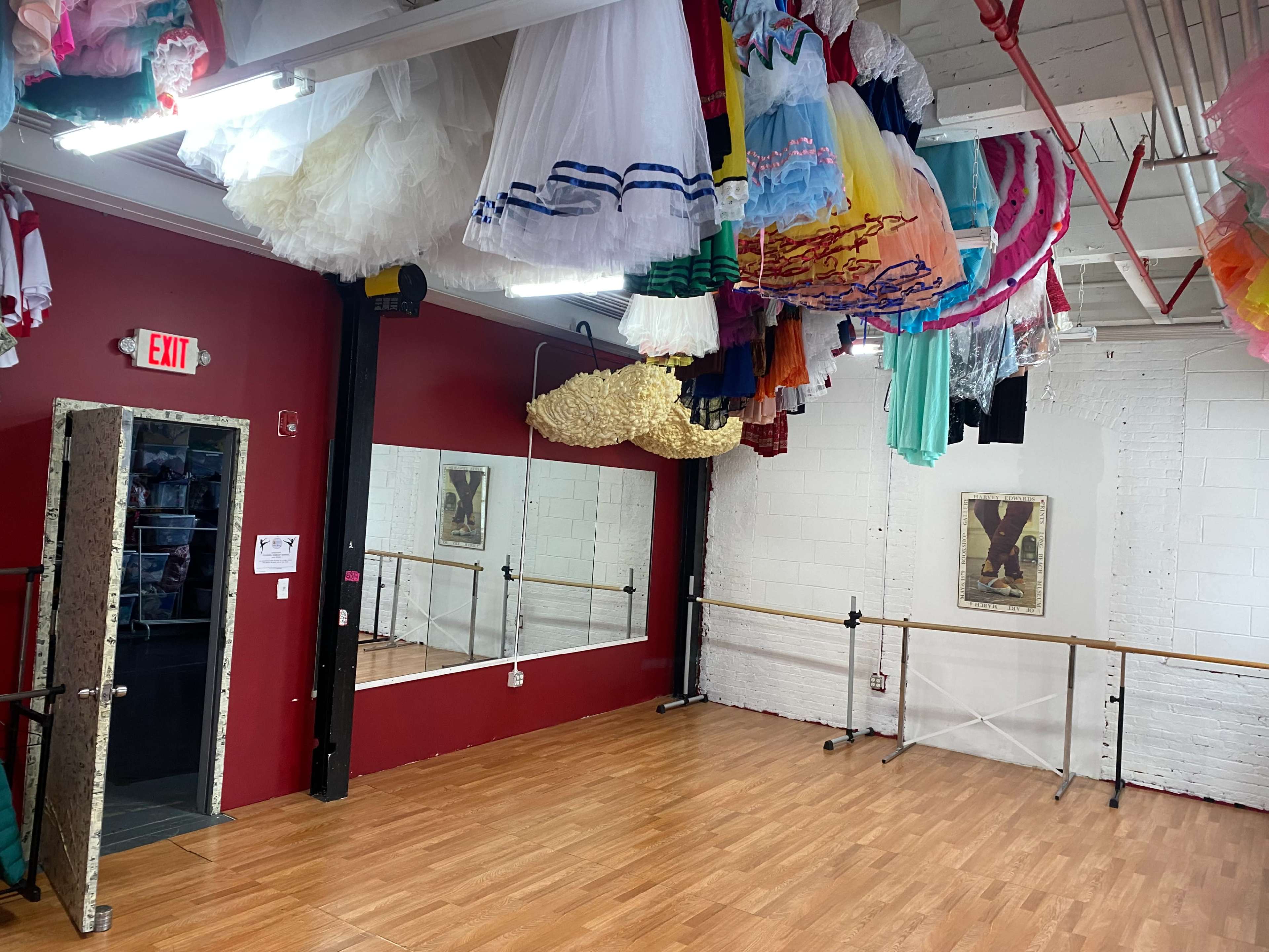 A dance studio with colorful costumes hanging from the ceiling and mirrors along one wall.
