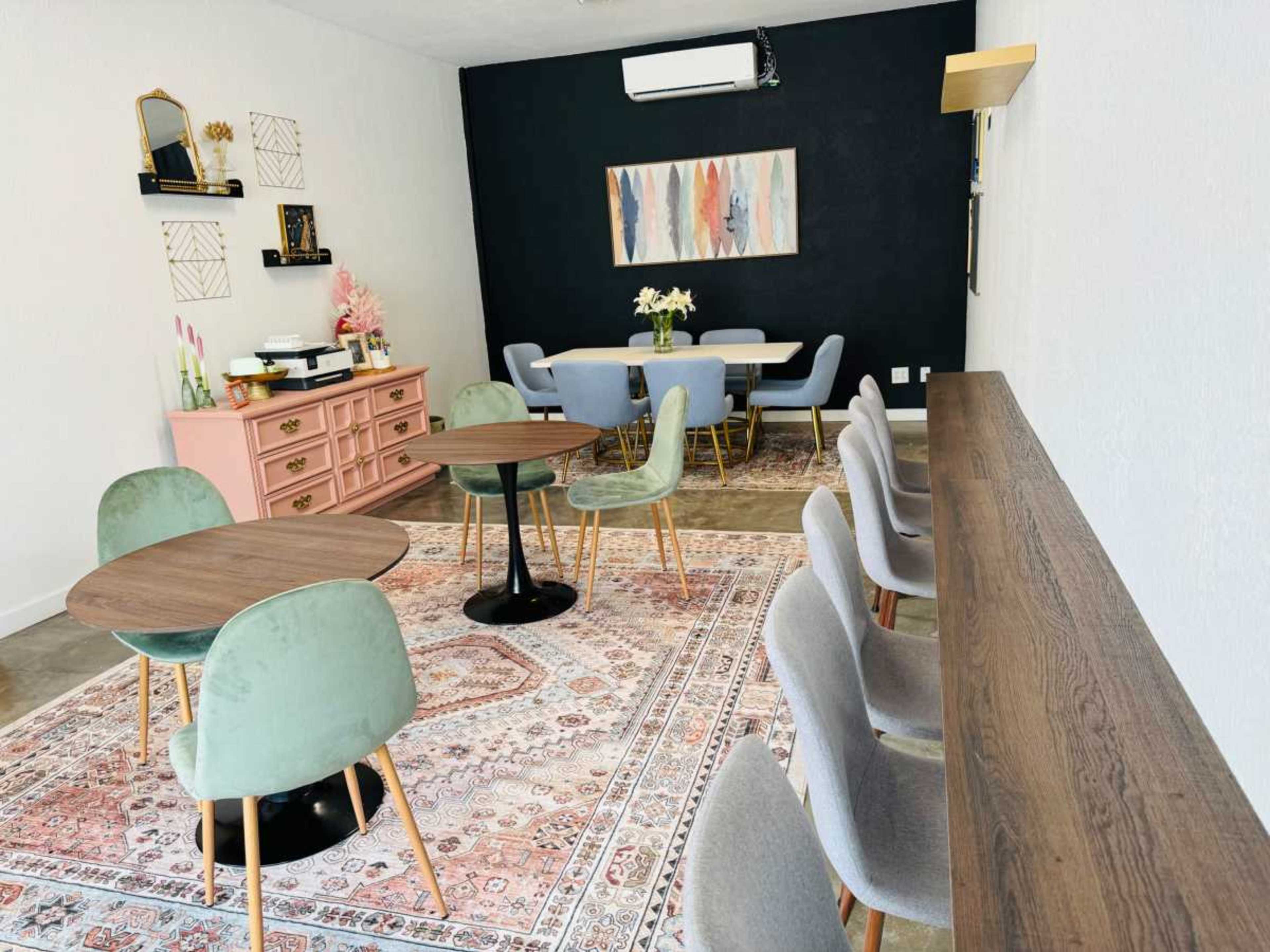 A cozy café space with a mix of round tables and chairs, a pink dresser, and a large artwork on the wall.