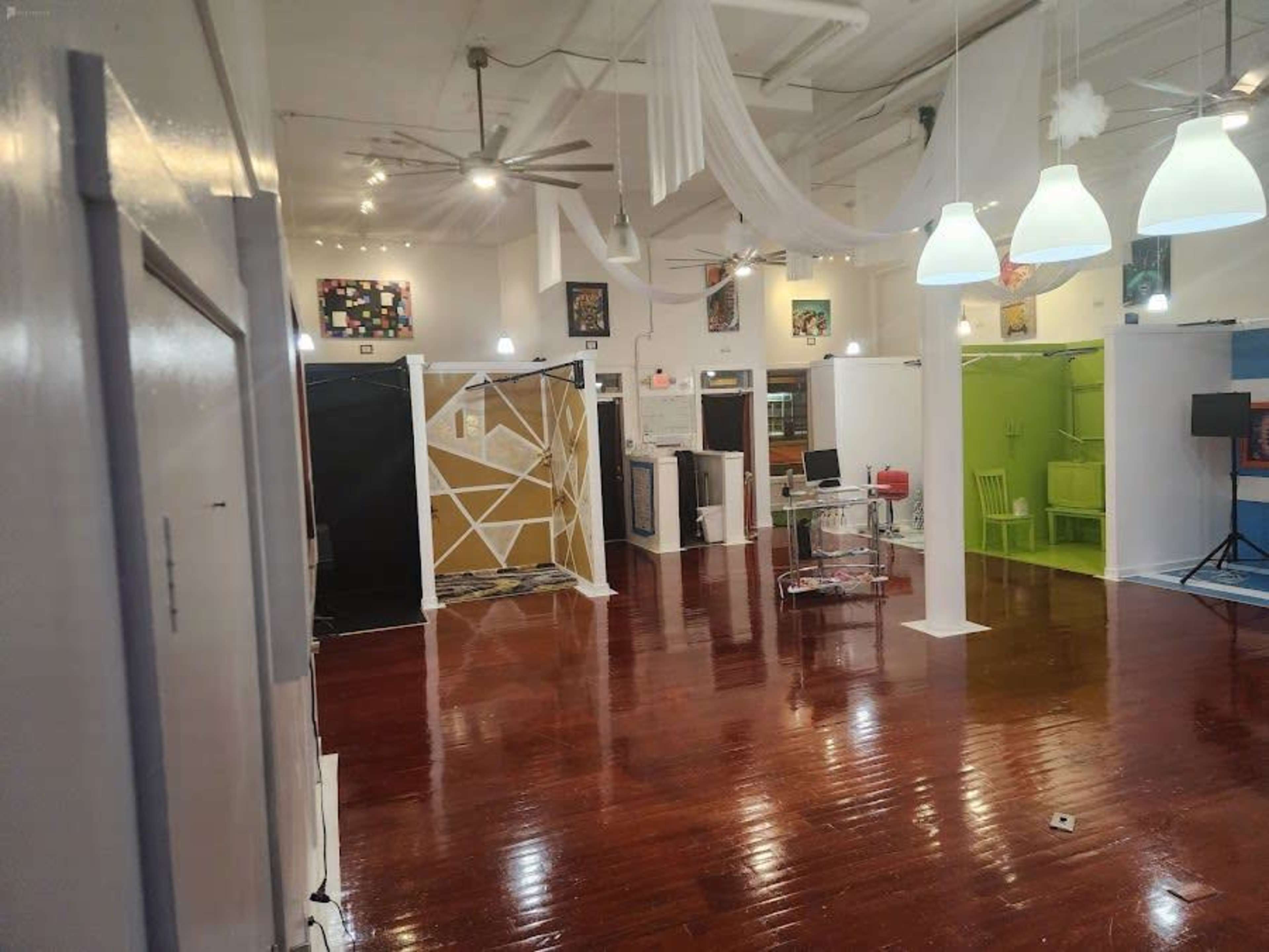 A spacious art studio with polished wooden floors, various colored partitions, and hanging light fixtures.
