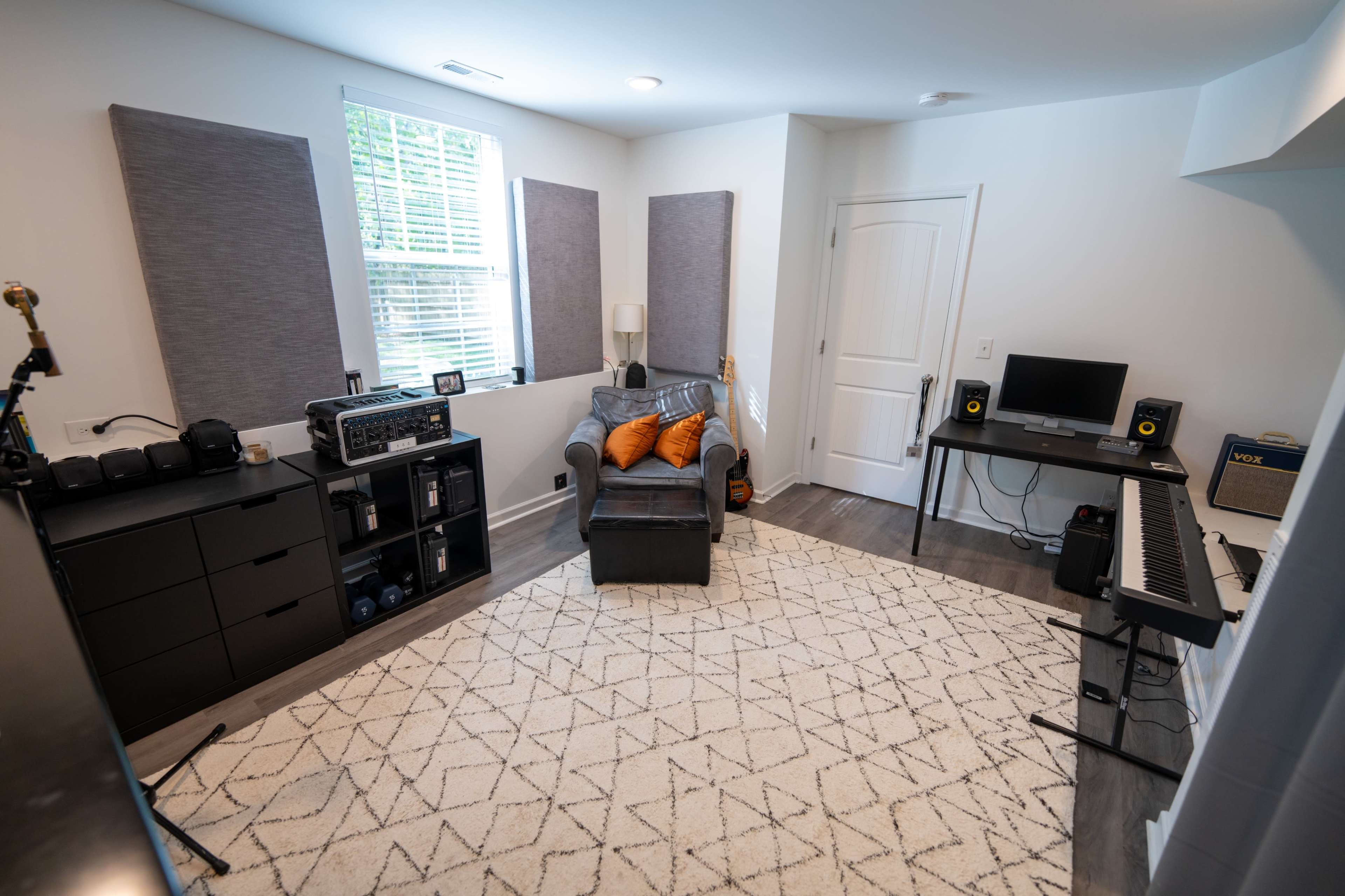 A cozy room with a gray sofa, a patterned rug, a keyboard, and shelves containing audio equipment.