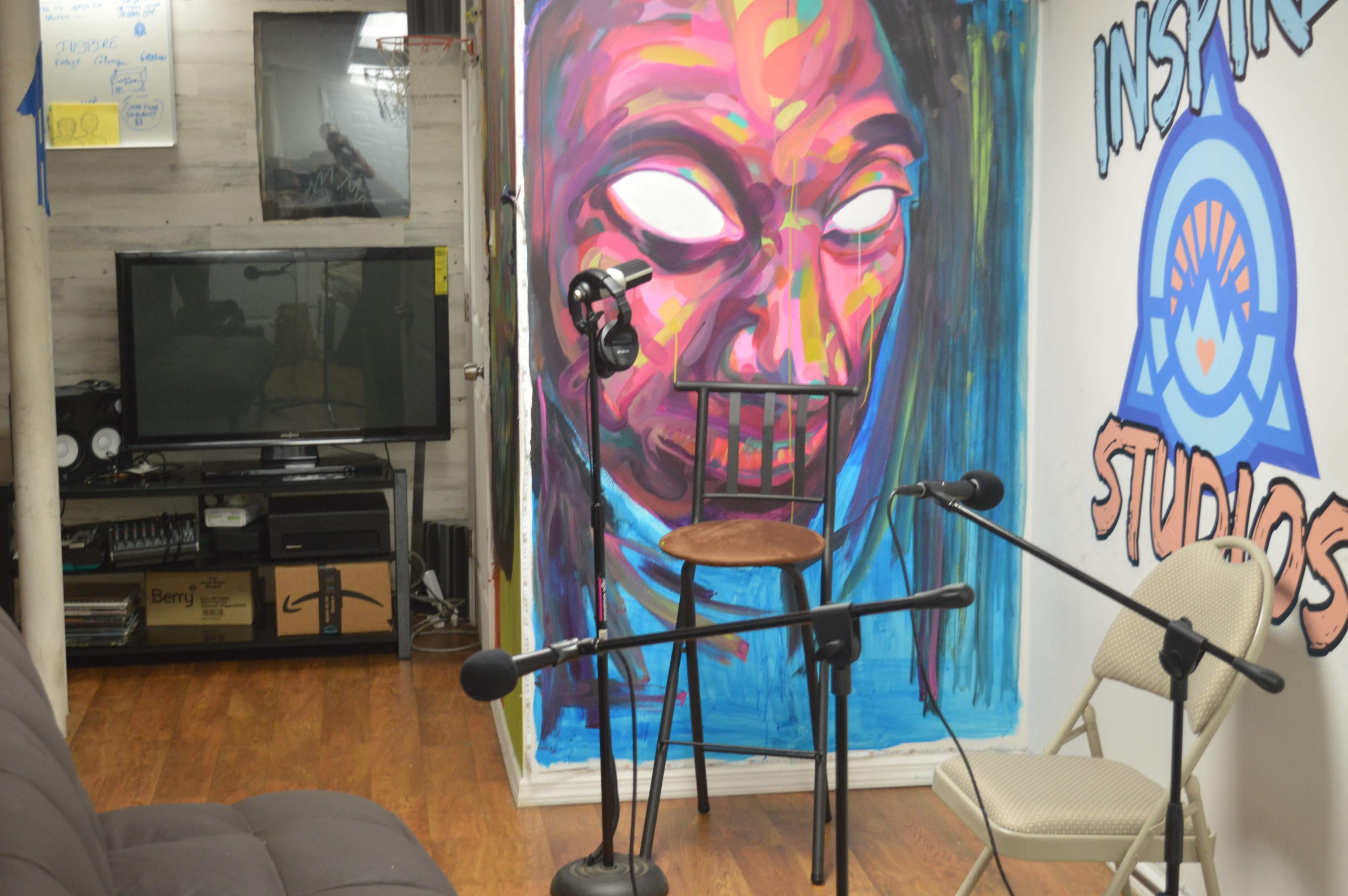 A studio space with a large mural featuring a face, a chair, and microphones arranged around the area.