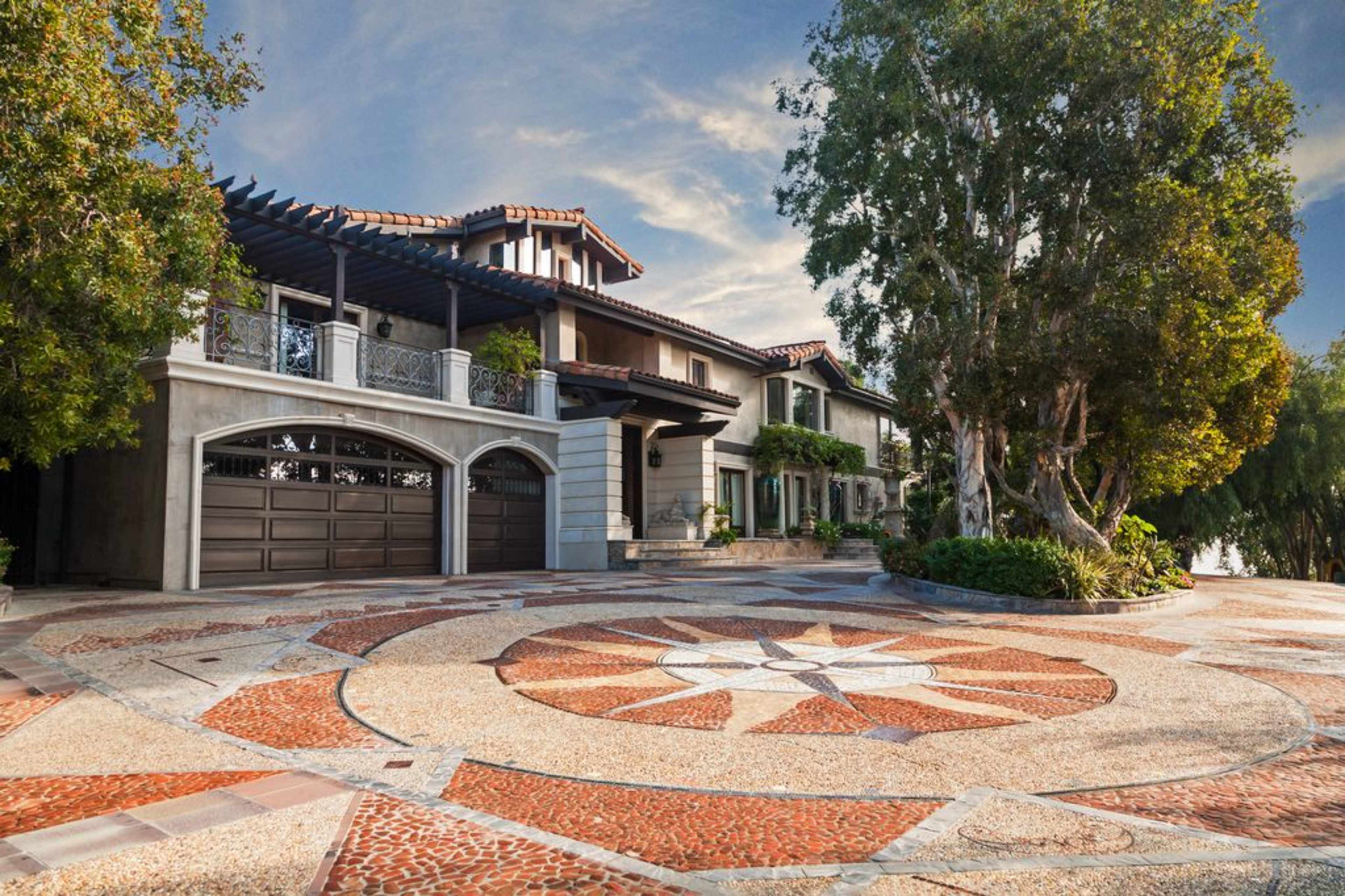 A large residential house with a tile roof and an ornate circular driveway featuring a stone pattern.