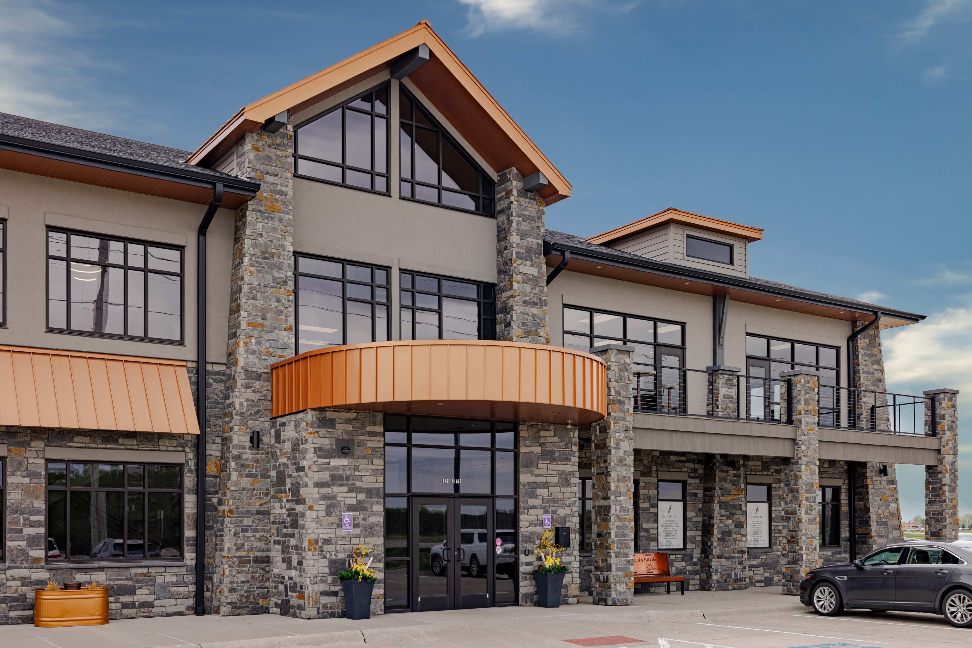 The image shows a modern stone and metal building with large windows and a prominent orange awning.